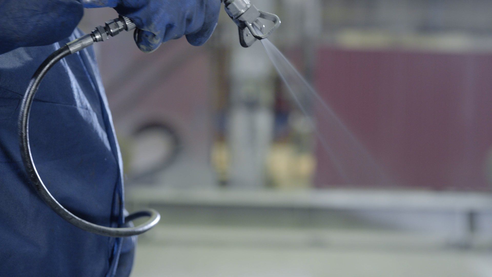 Blue-gloved worker spraying paint in an indoor spray paint facility