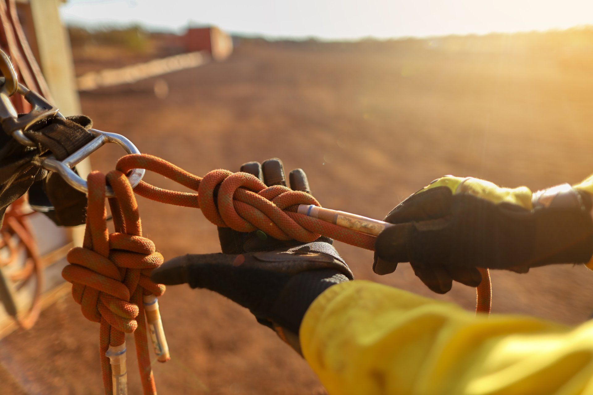 Person in safety gear tying a figure-eight knot on a rope. Outdoor, sunny setting.