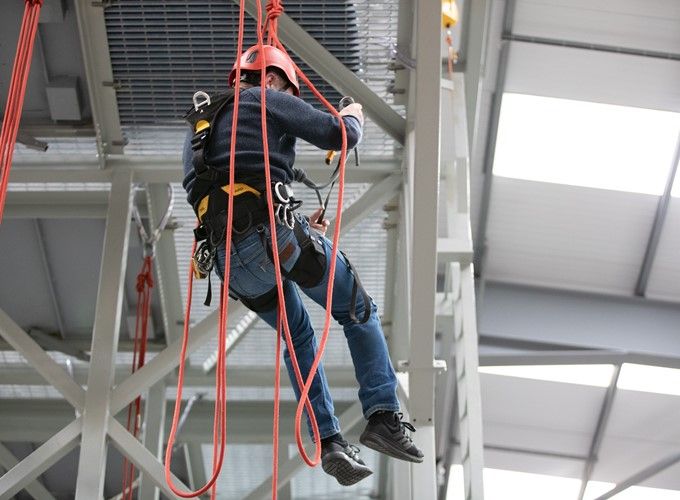A man wearing a helmet is climbing a rope in a building