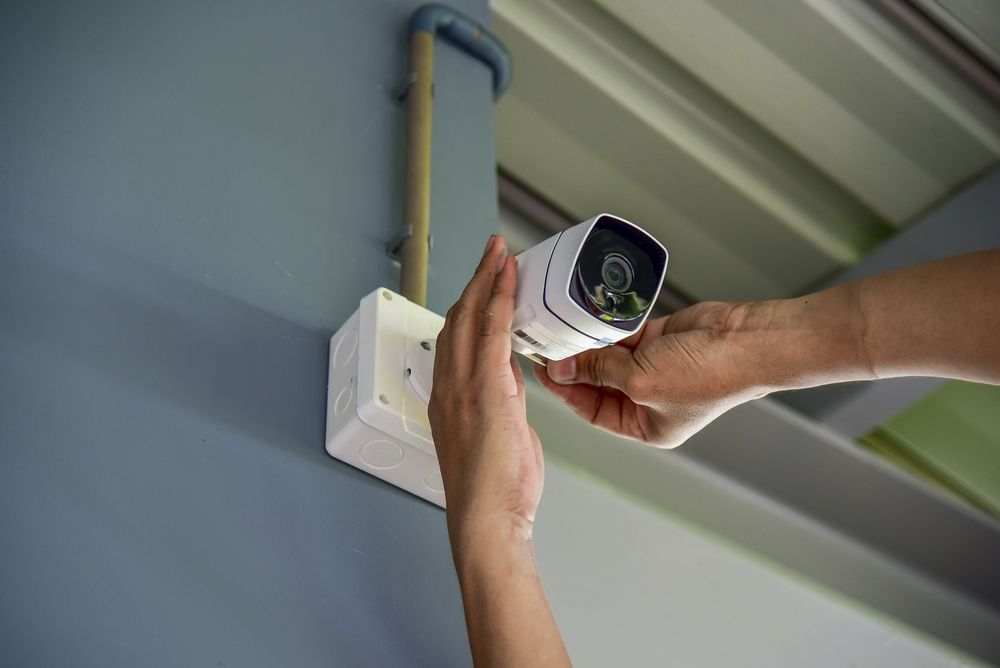 Man Is Installing A Security Camera On A Wall With Both Hands — Ontime Locksmiths & Security In Ocean Shores, NSW