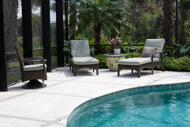 Outdoor seating area with pool. Three wicker chairs with cushions on a white patio. Green plants and a blue pool. Outdoor seating area with pool. Three wicker chairs with cushions on a white patio. Green plants and a blue pool.