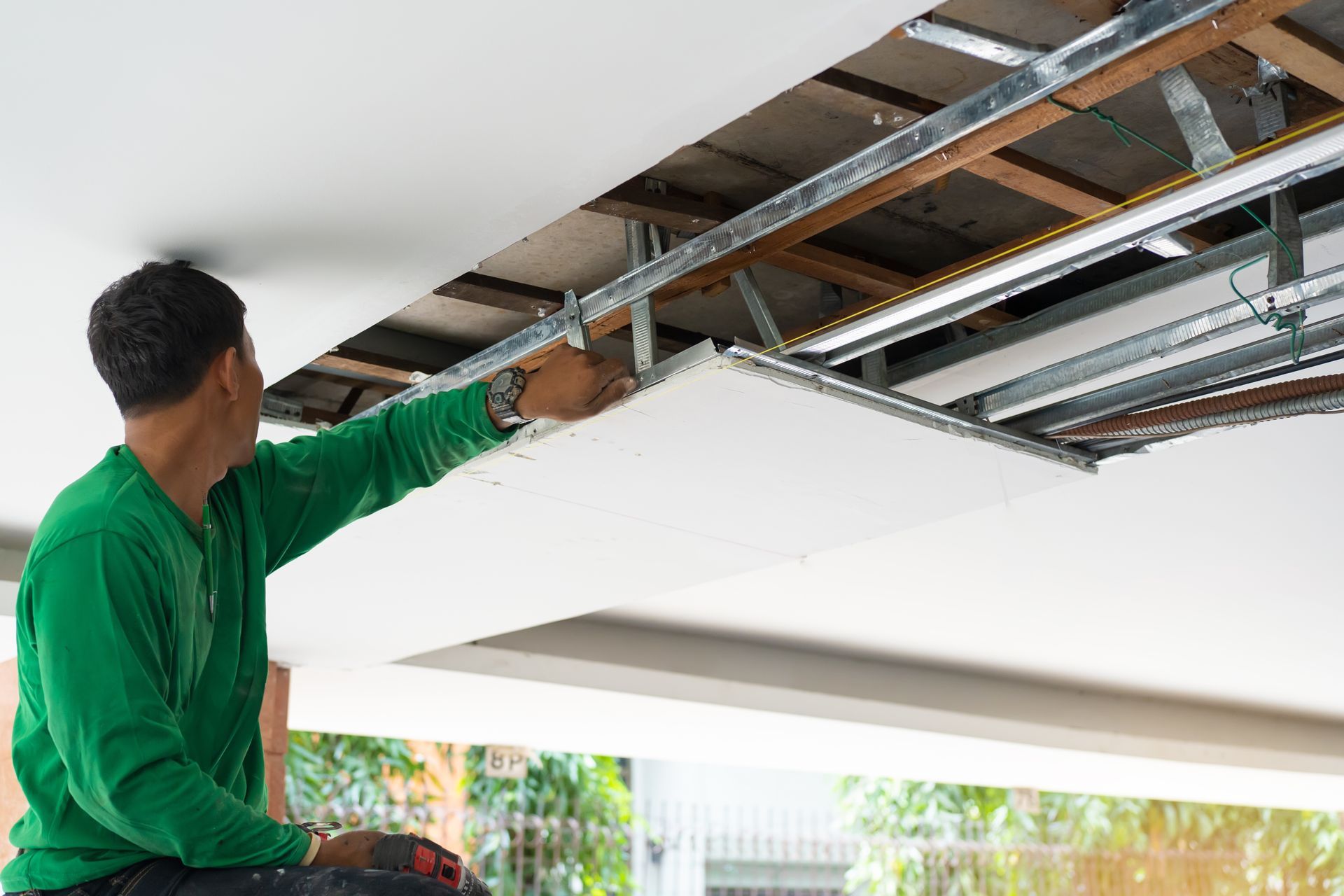 A man in a green shirt is working on a ceiling.