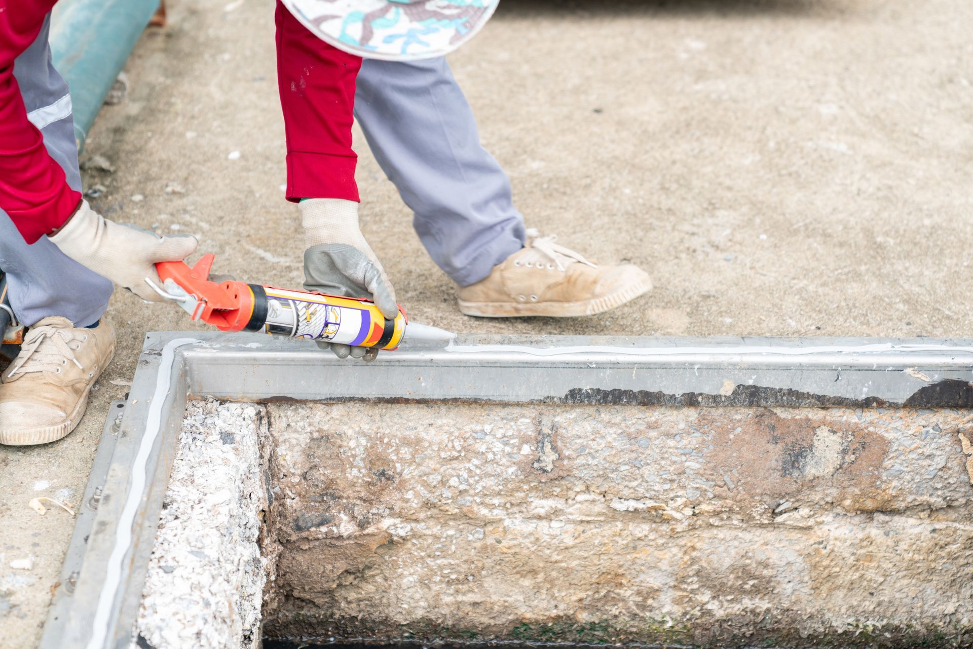 A person is applying silicone sealant to a manhole cover.