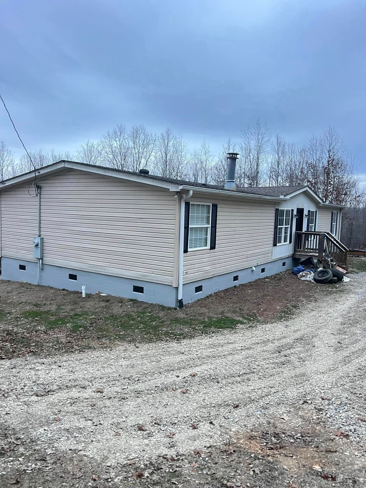 Single-story beige mobile home with white trim on a gravel driveway under a cloudy sky