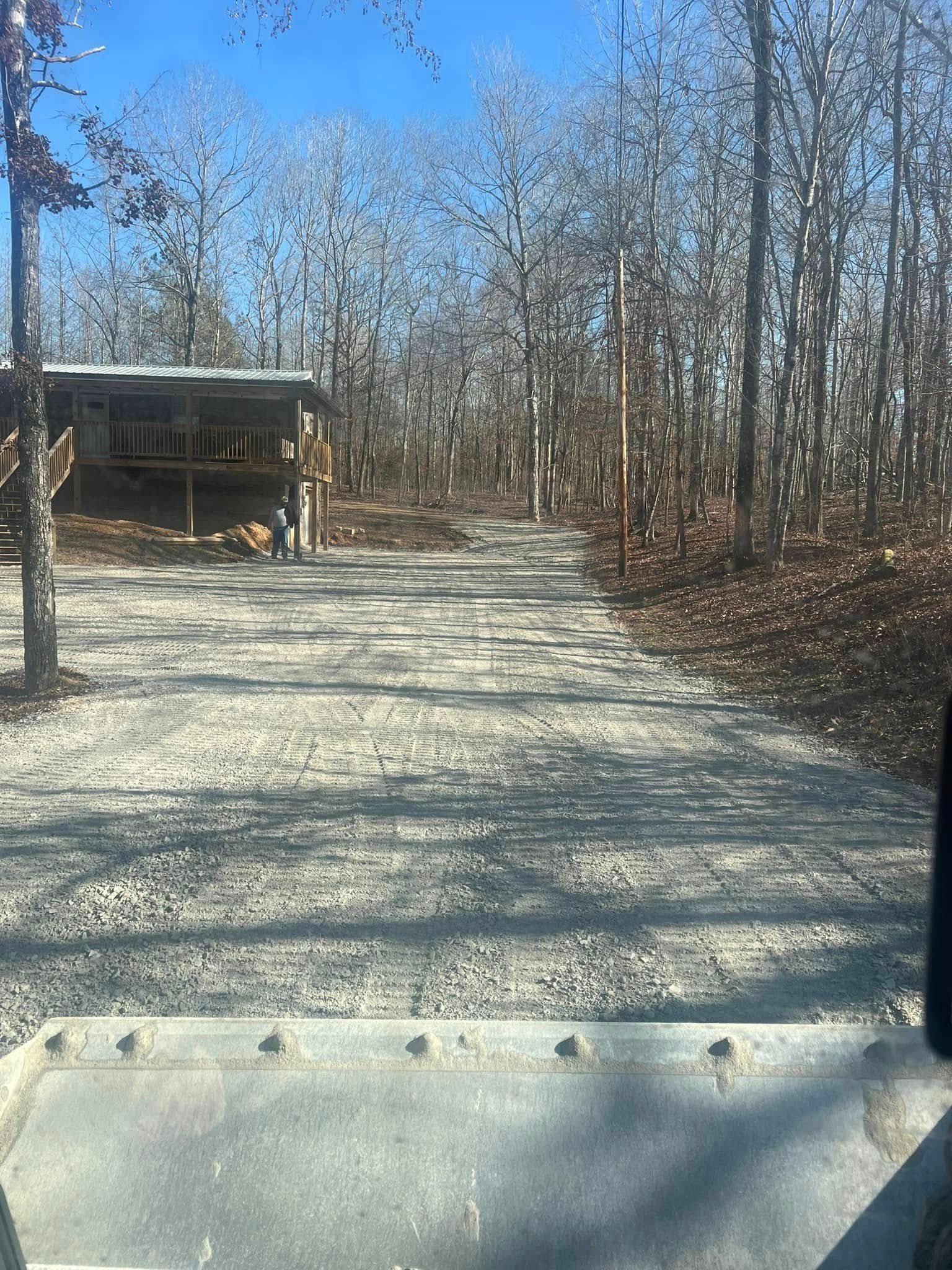 Gravel driveway leading to a small building and leafless trees on a sunny day