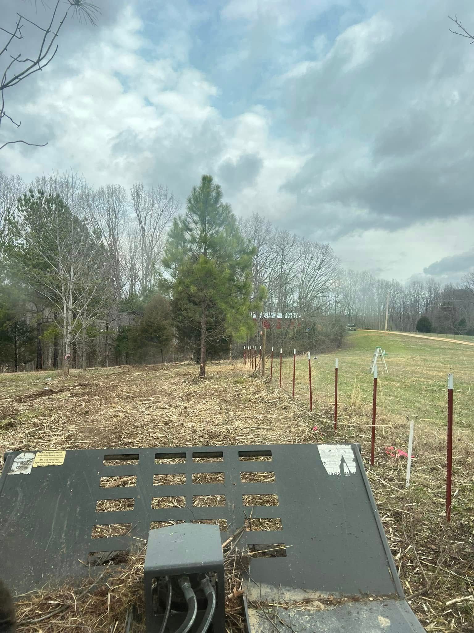 Outdoor platform overlooking a grassy field and cloudy sky, with trees and a gray metal surface in the foreground