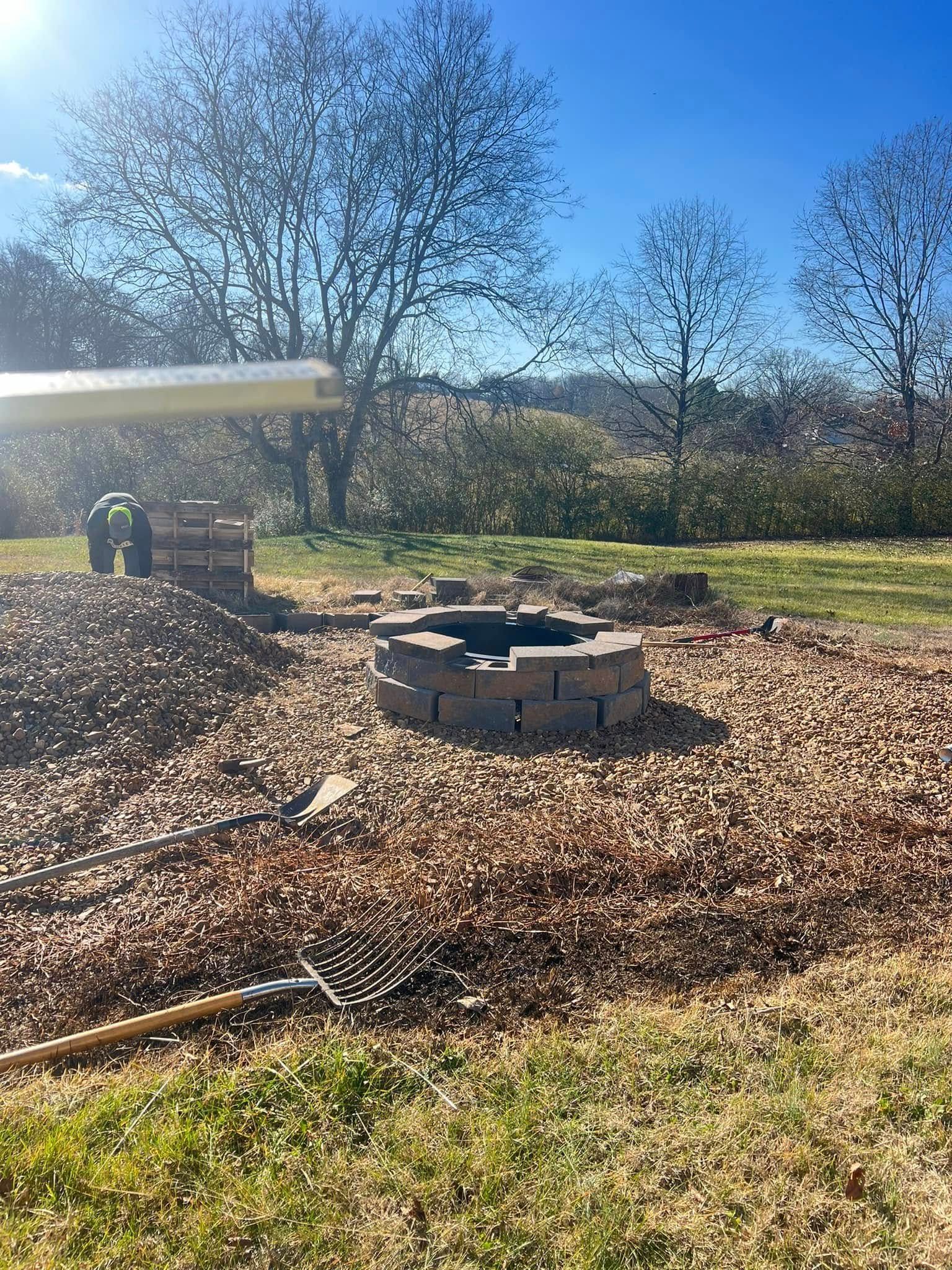 Outdoor yard with a circular stone fire pit being built on a sunny day