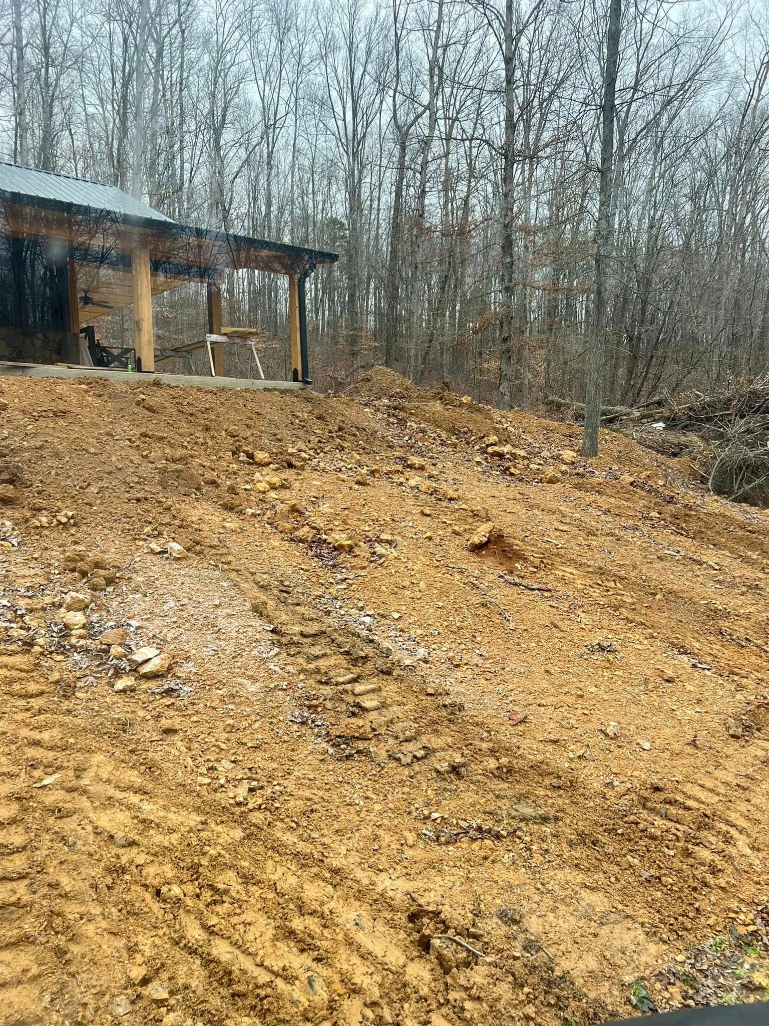 Large muddy dirt slope beside a small shed in a leafless wooded area