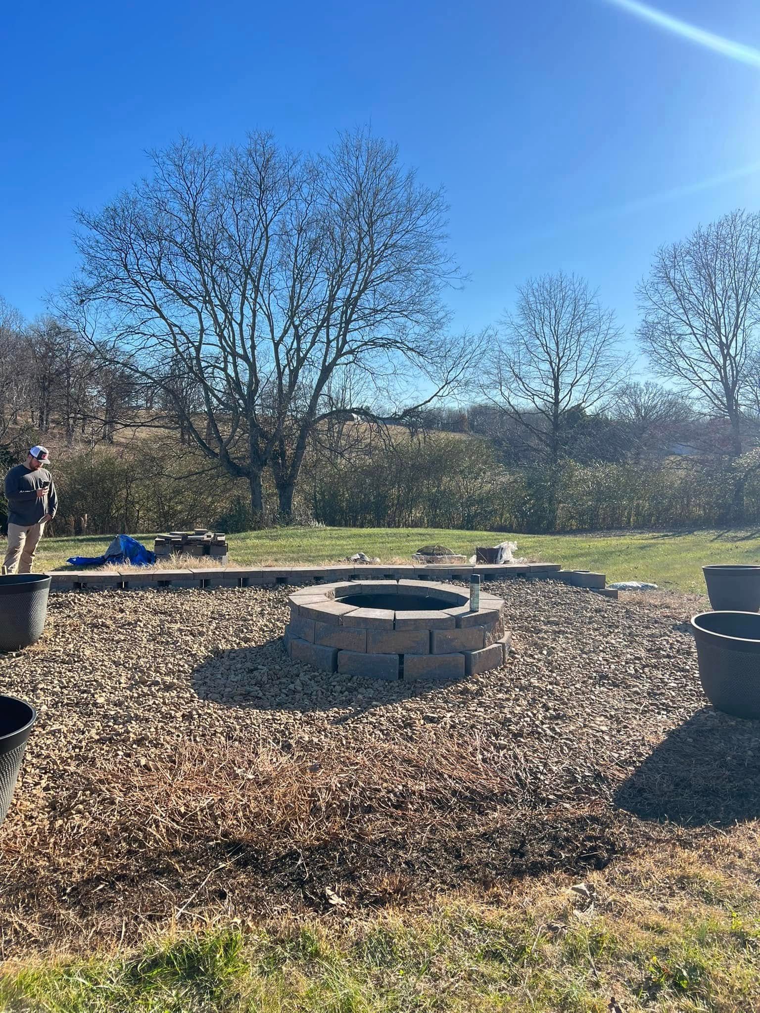 Backyard fire pit surrounded by mulch, with trees and a clear blue sky on a sunny day