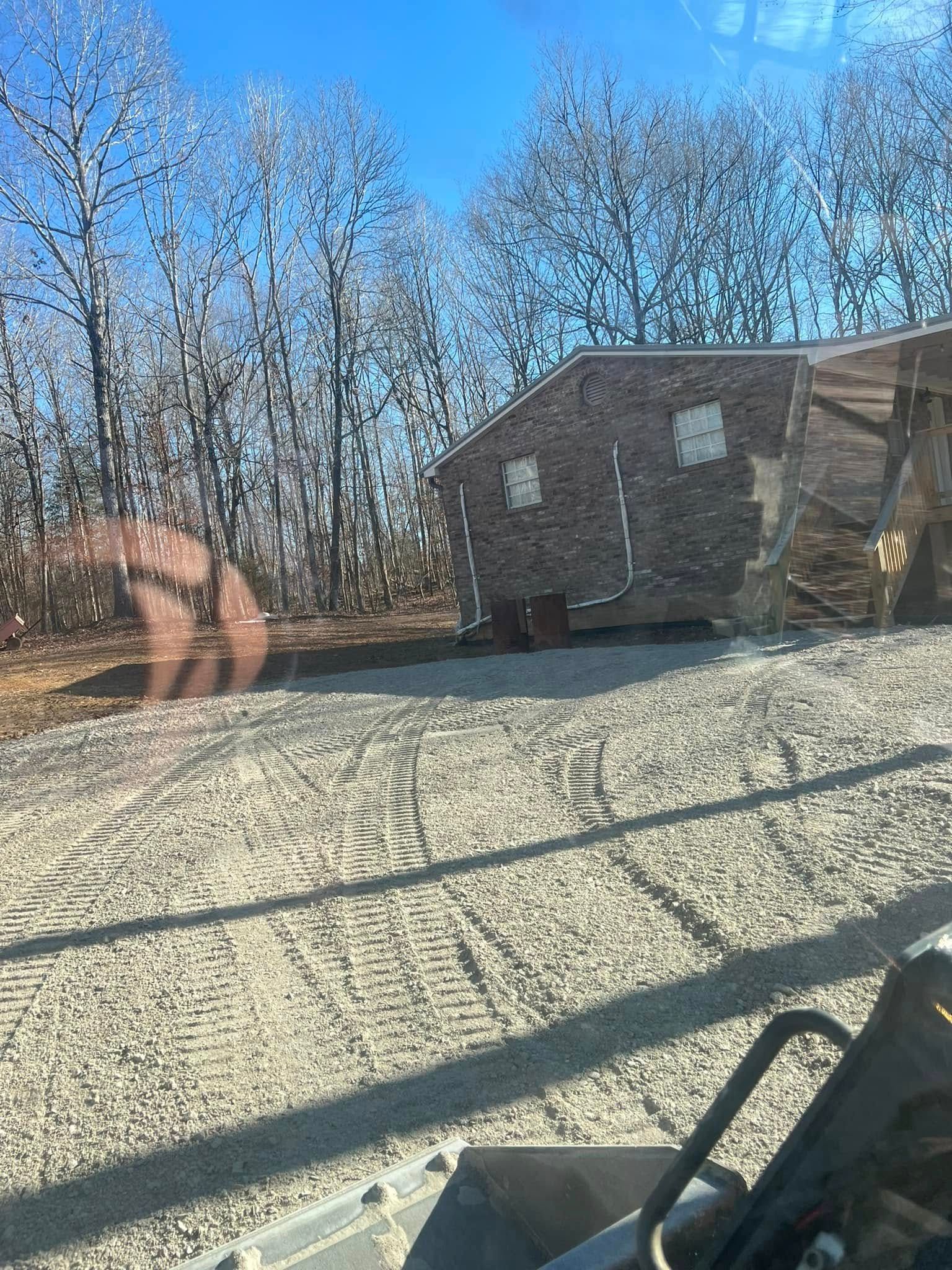 Gravel yard with a brown shed, leafless trees, and a clear blue sky