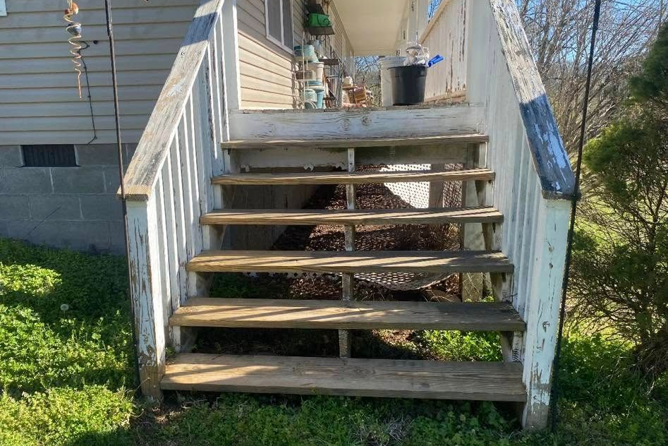 Wooden backyard stairs with white railings leading up to a house entrance
