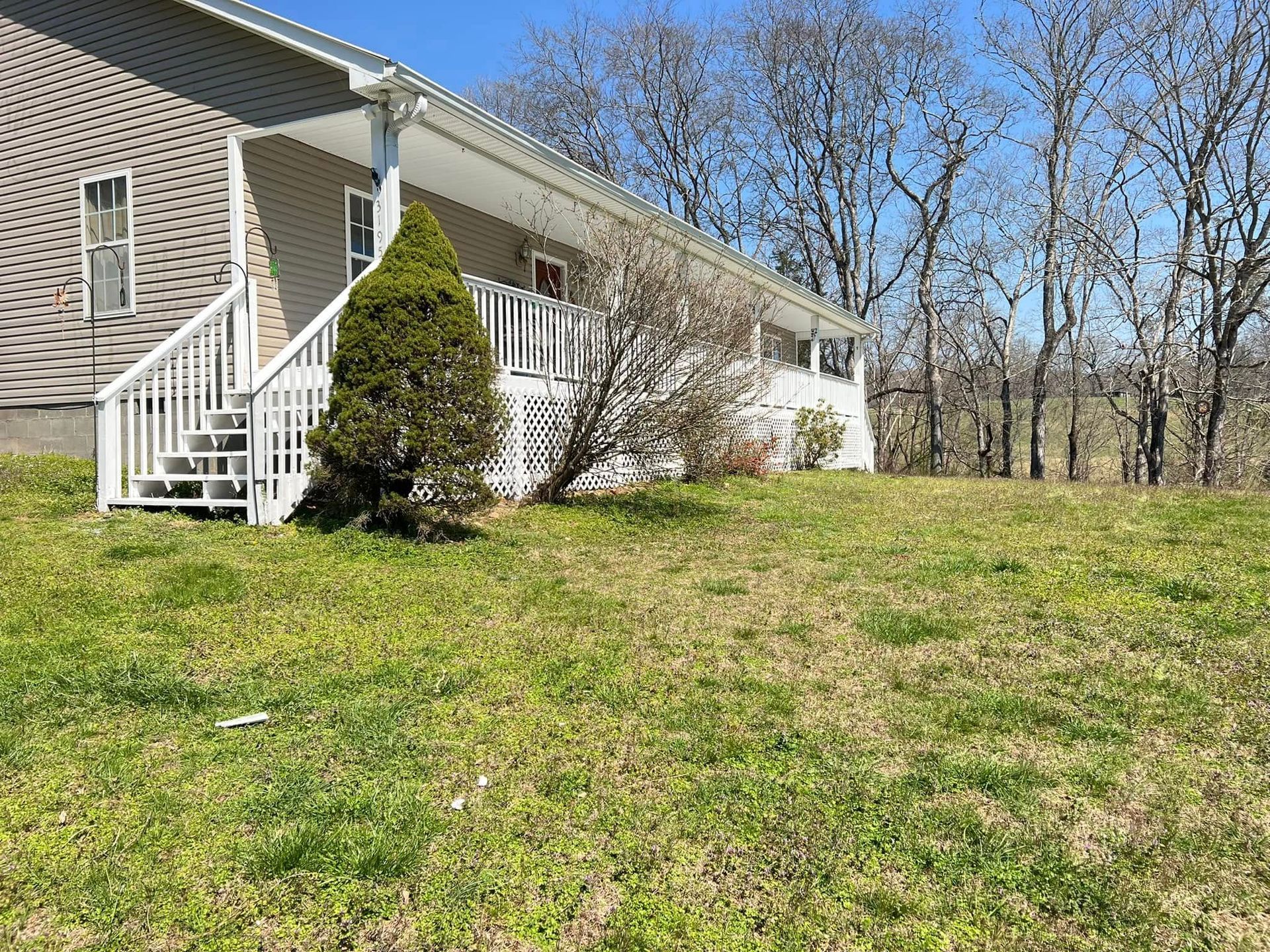 House exterior with white stairs, tan siding, and a grassy yard beside leafless trees