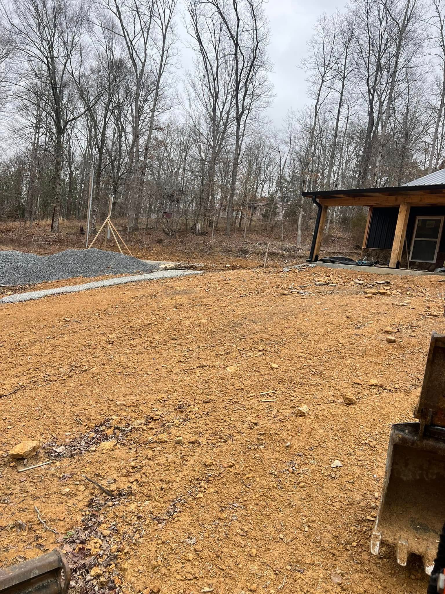 Outdoor gravel yard with bare trees and a small shed or shelter on the right