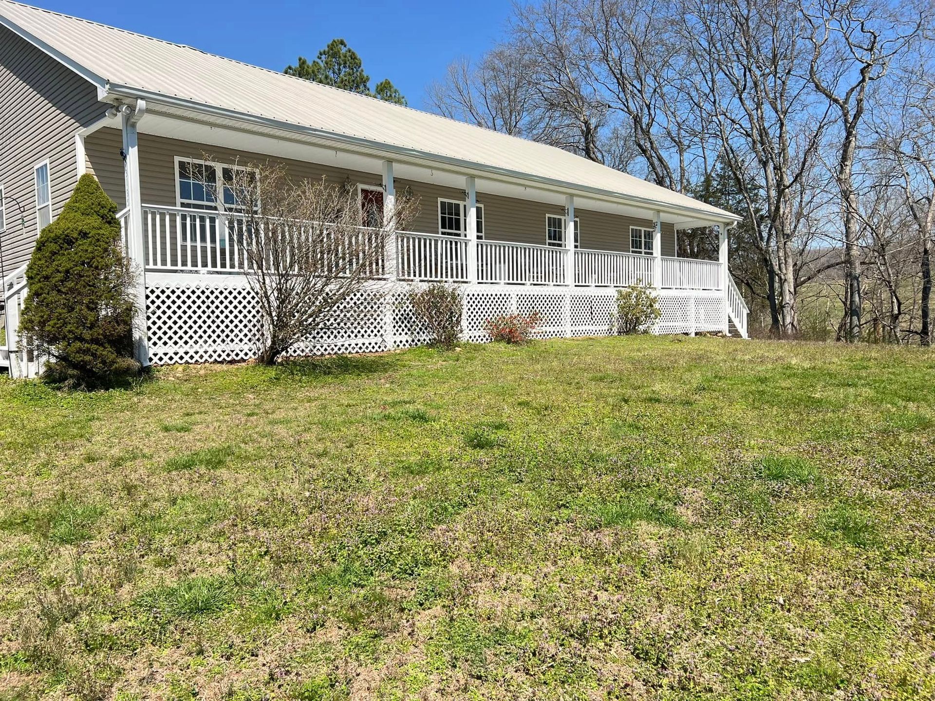 Single-story white house with a porch, set on a grassy hill under a clear blue sky.