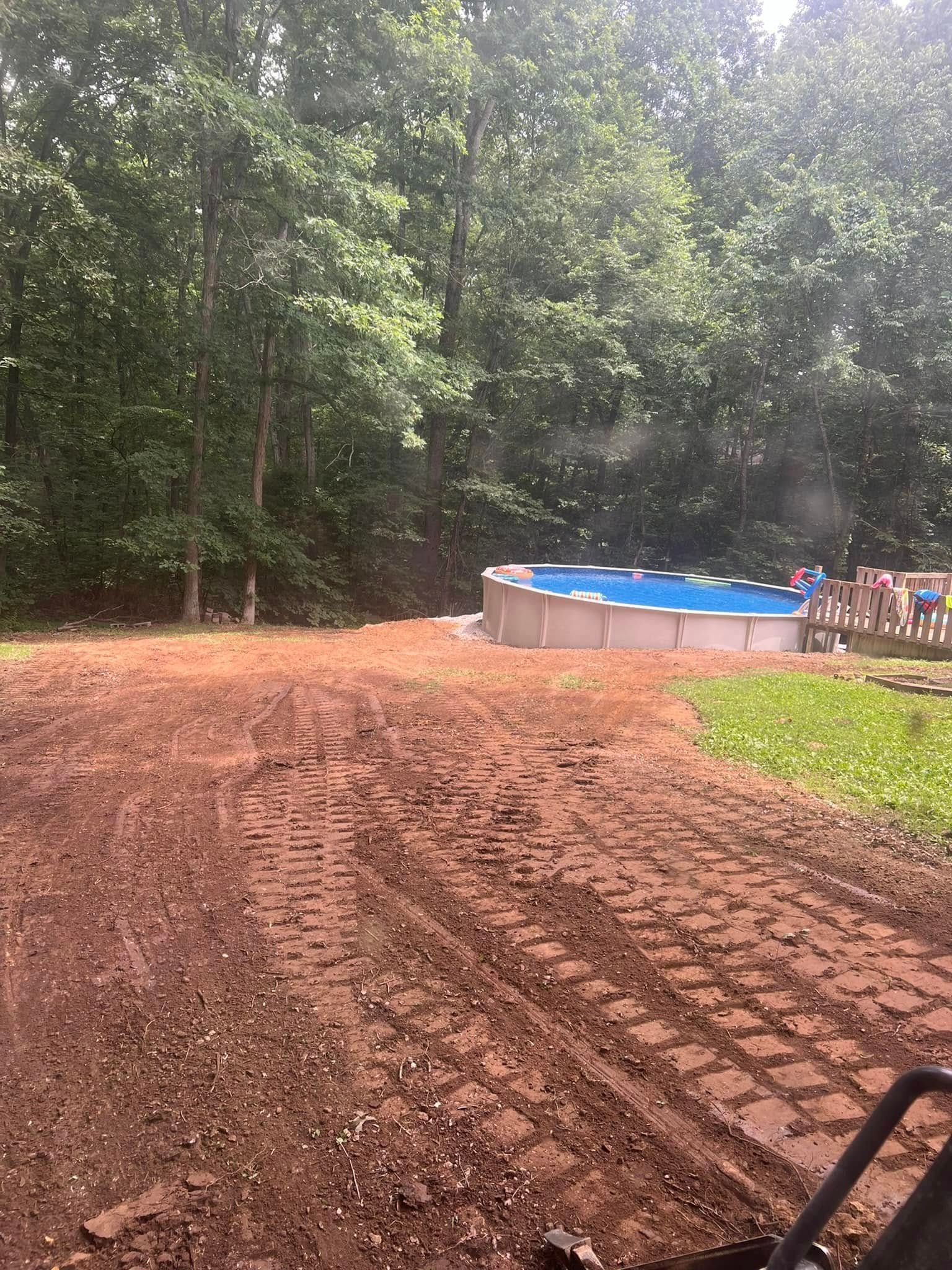 Freshly tilled muddy yard beside trees, with a blue above-ground pool in the background.