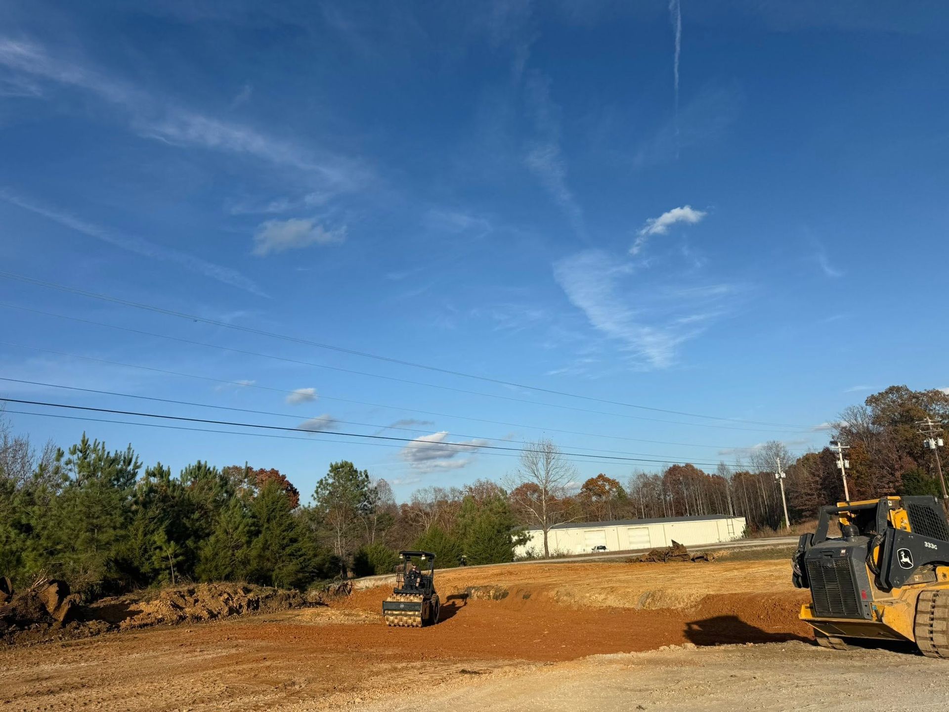 Bulldozers on a dirt lot under a clear blue sky, with trees and a building in the background