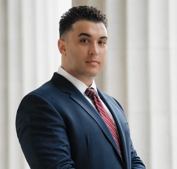 Man in navy suit and red tie standing indoors against a bright window backdrop