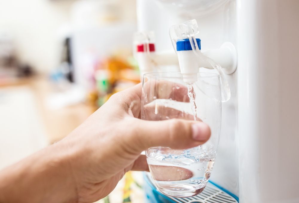 A Person Is Pouring Water Into A Glass From A Water Dispenser — Cairns Clear Water Company In Westcourt, QLD