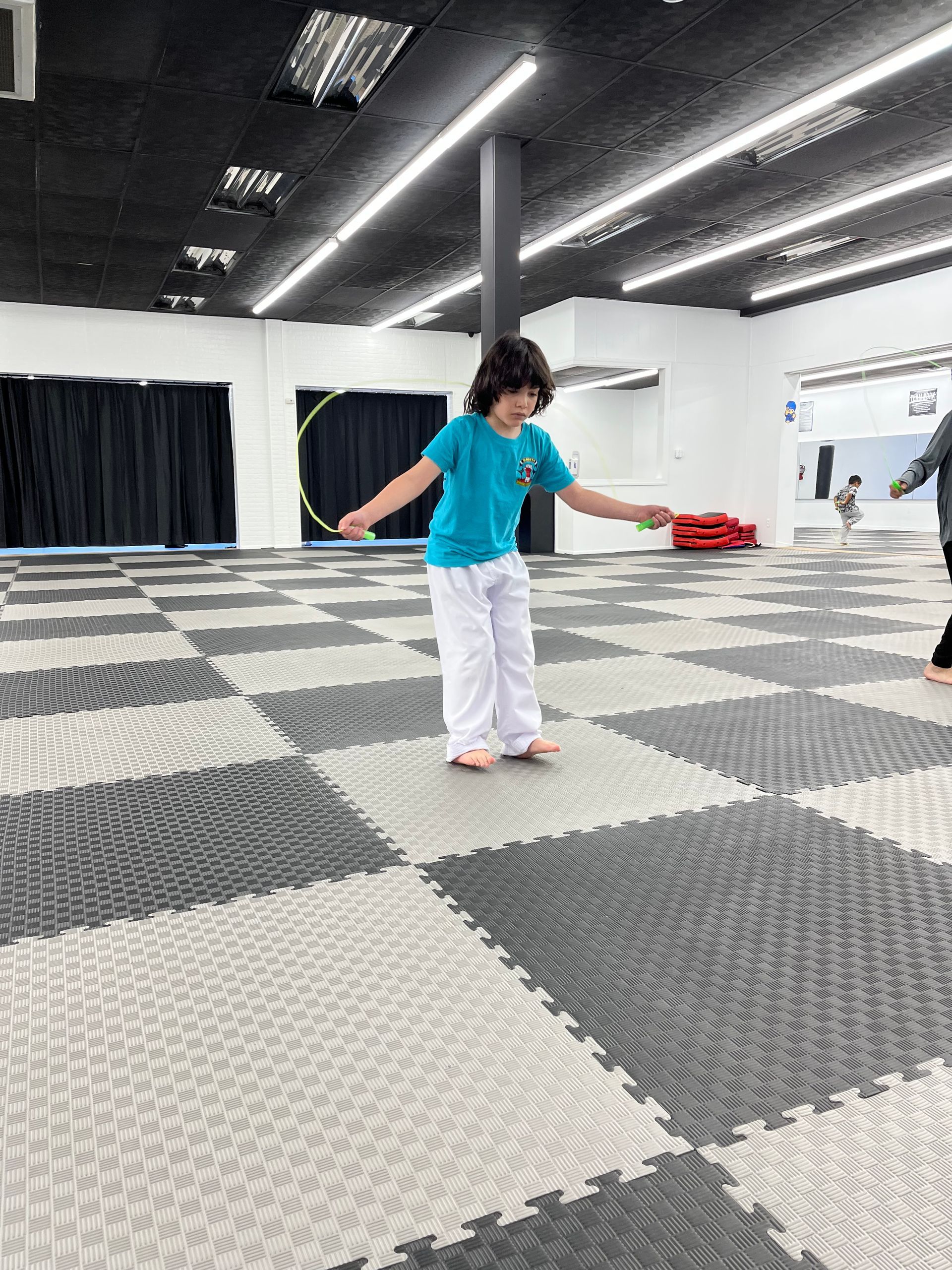 Child in a blue shirt and white pants balancing in a large studio with checkered foam floor mats.
