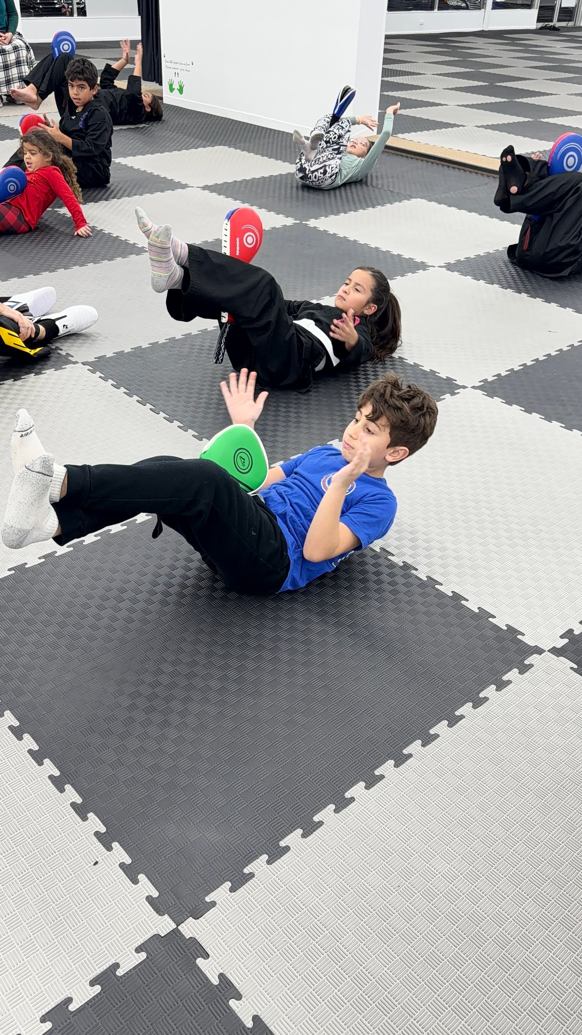 Four martial artists in uniforms, posed in a dojo, fists clenched, looking at camera.
