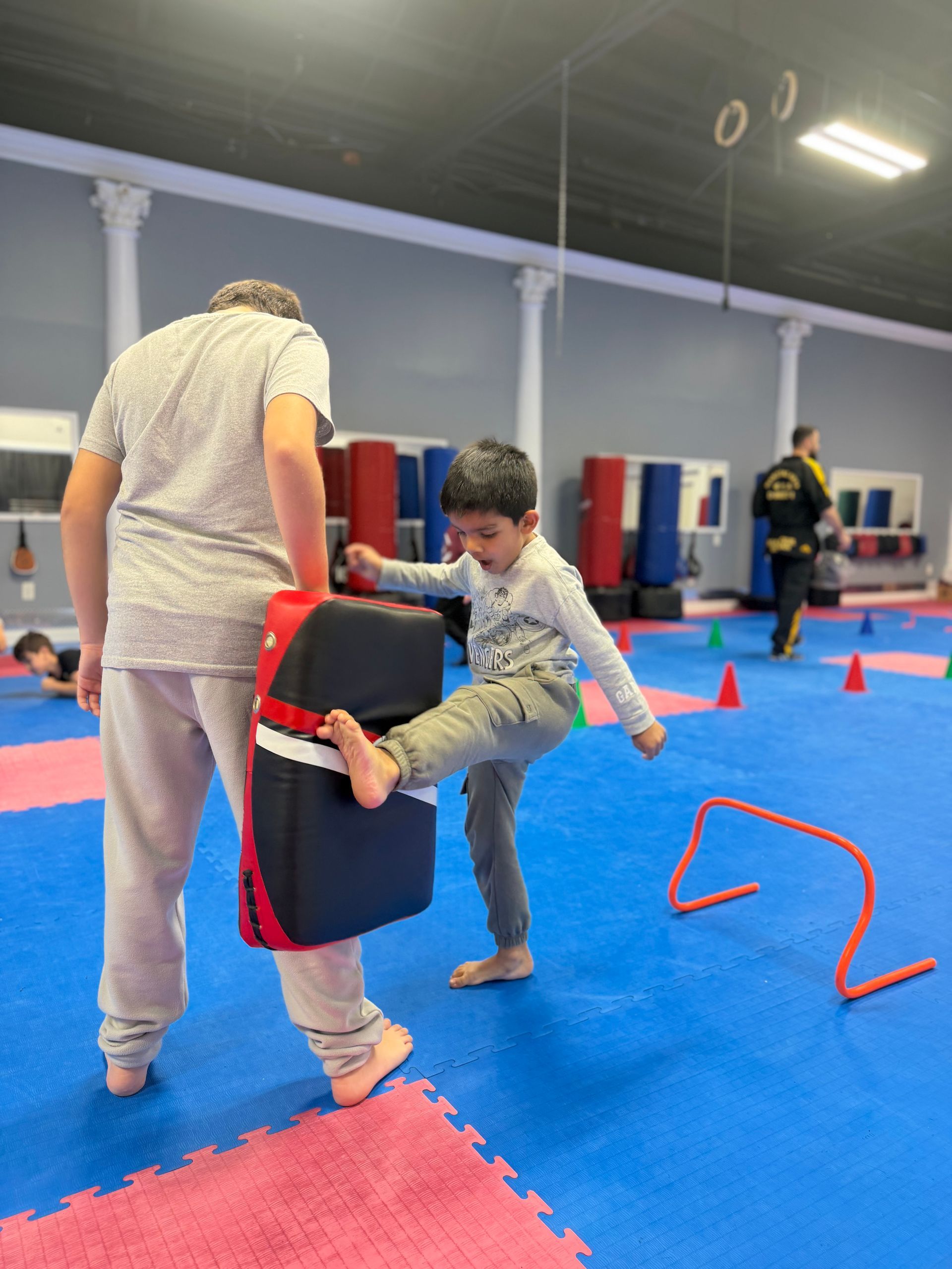 Two people practicing kickboxing drills on blue mats with red cones and training gear.