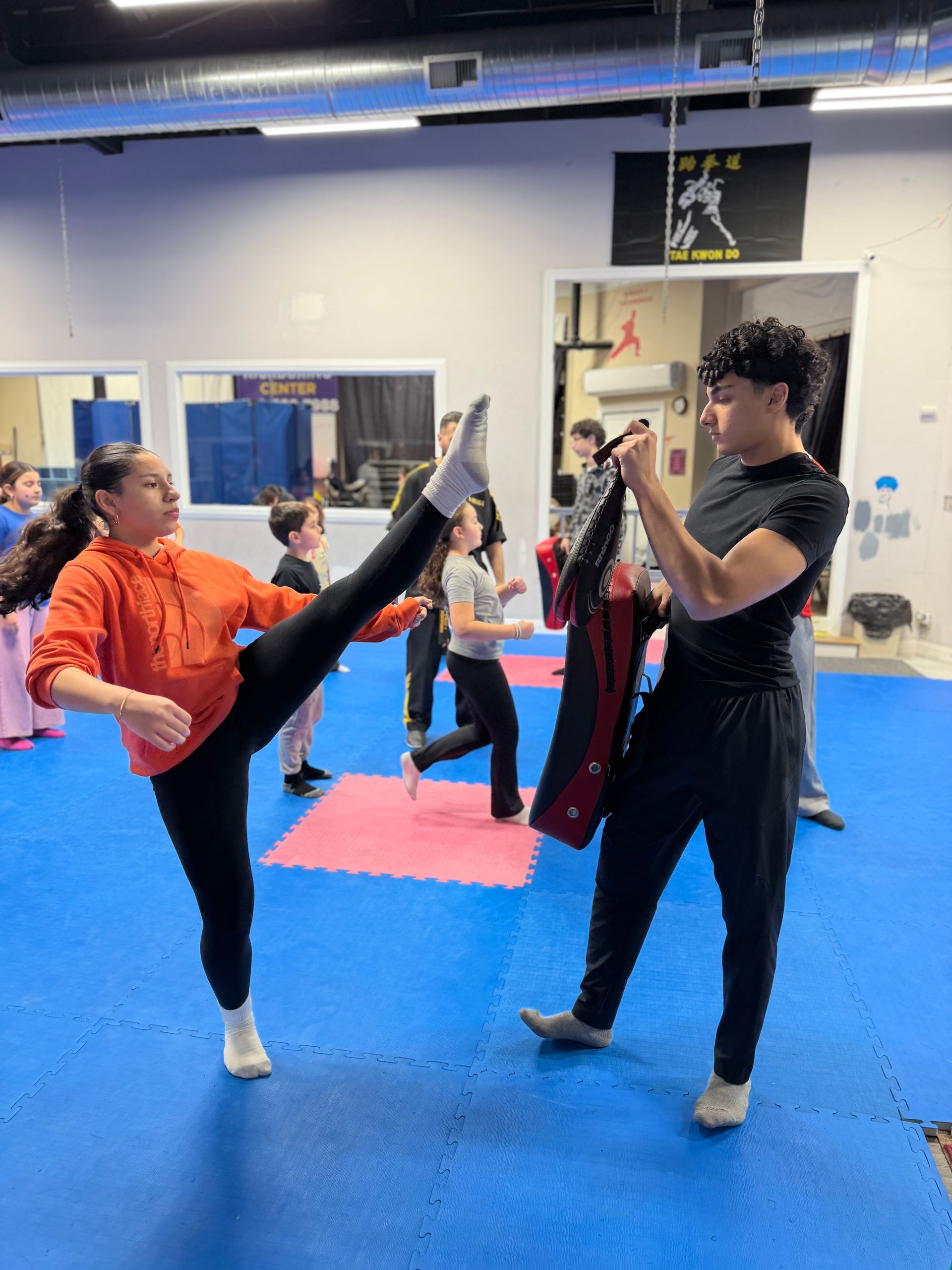 Martial arts class with students practicing high kicks on blue mats in a gym