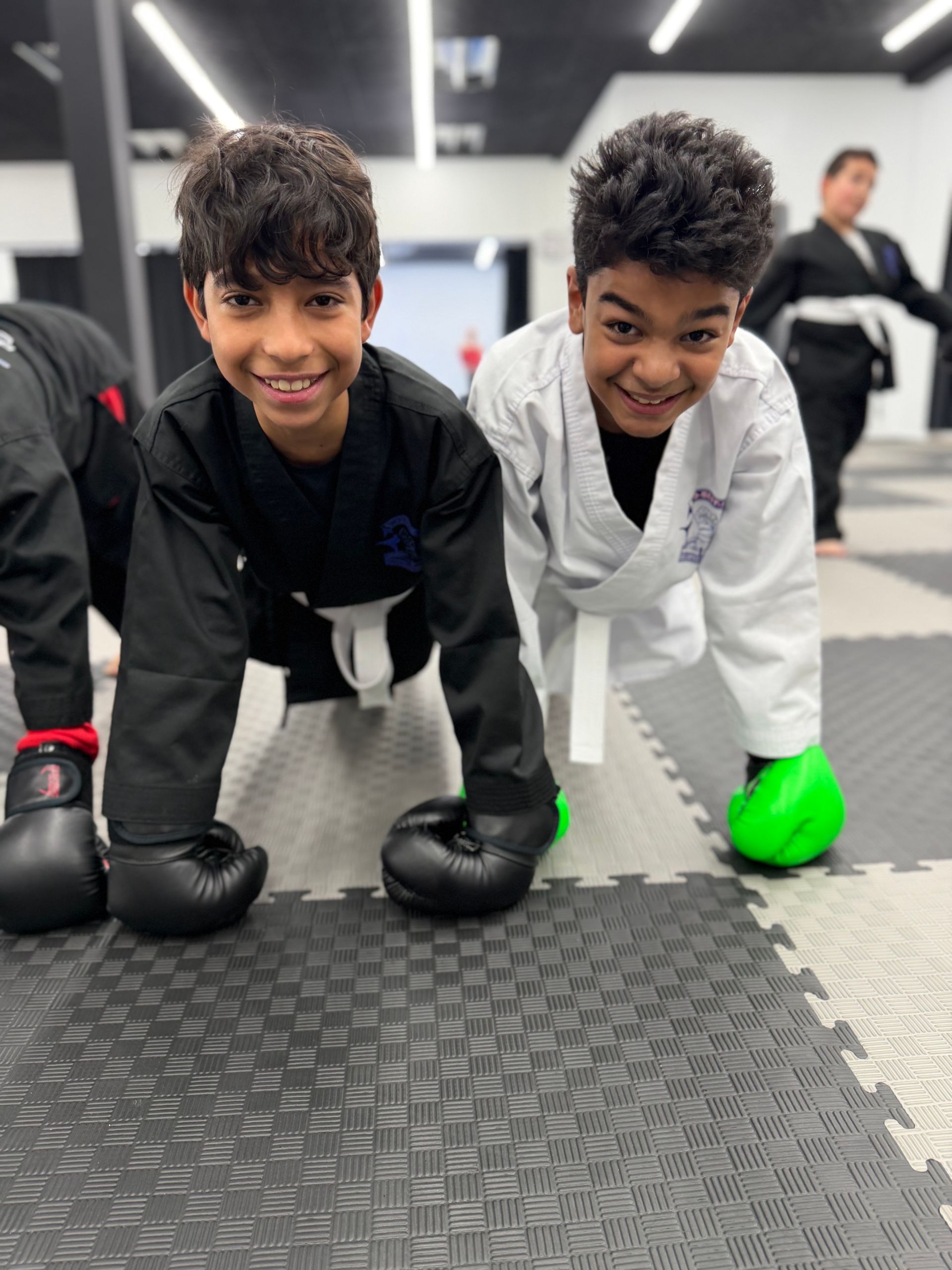 Four martial artists in uniforms, posed in a dojo, fists clenched, looking at camera.