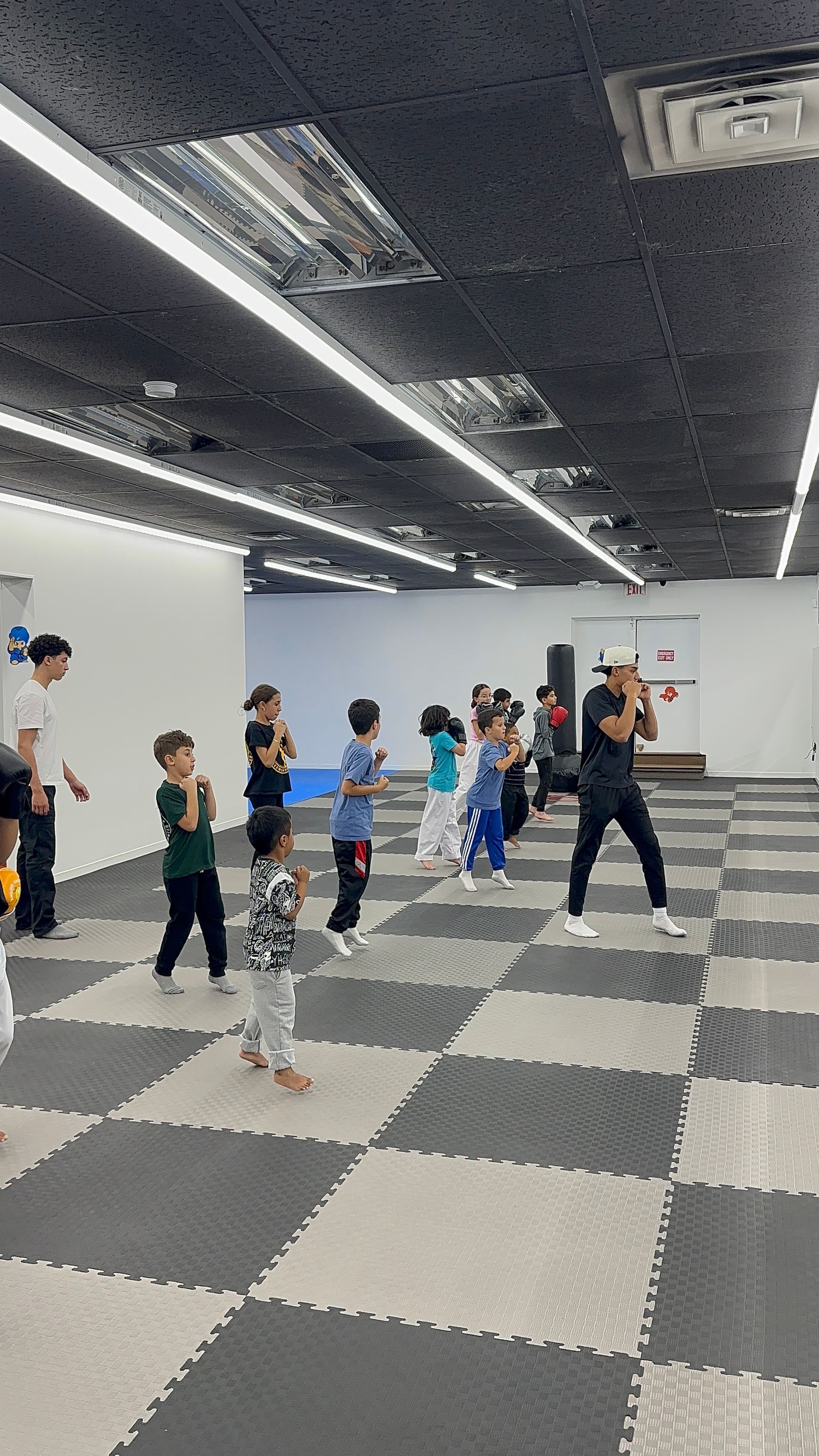 Children following an instructor in a dance class on a checkered floor in a studio