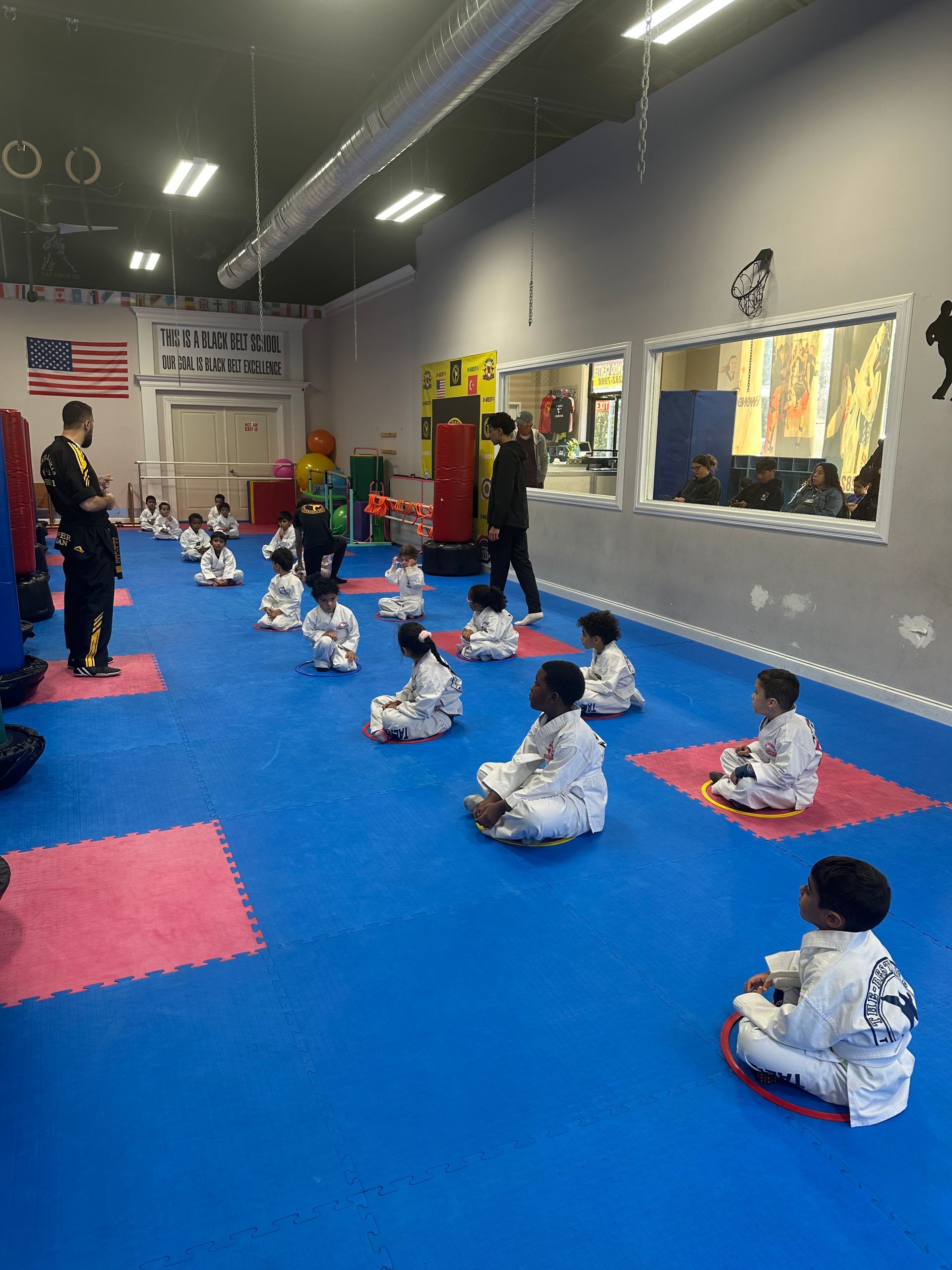 Martial arts class with children in white uniforms sitting on blue mats in a training studio