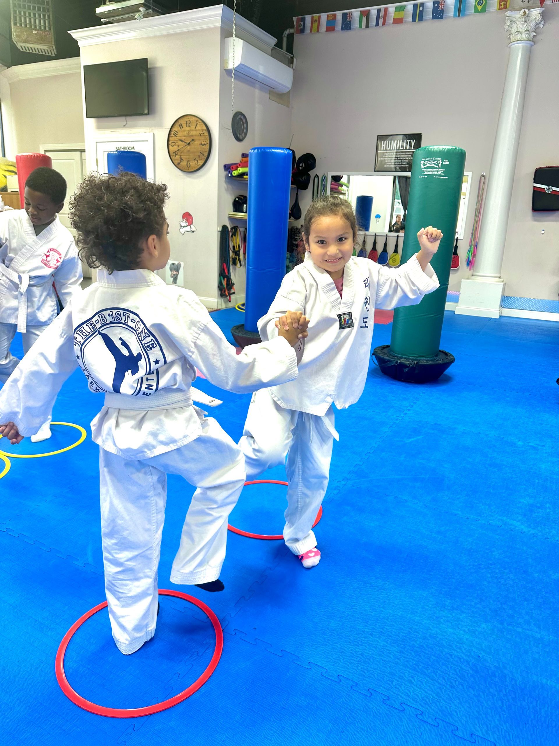 Children practicing martial arts in white uniforms on a blue mat with colored hoops in a bright studio