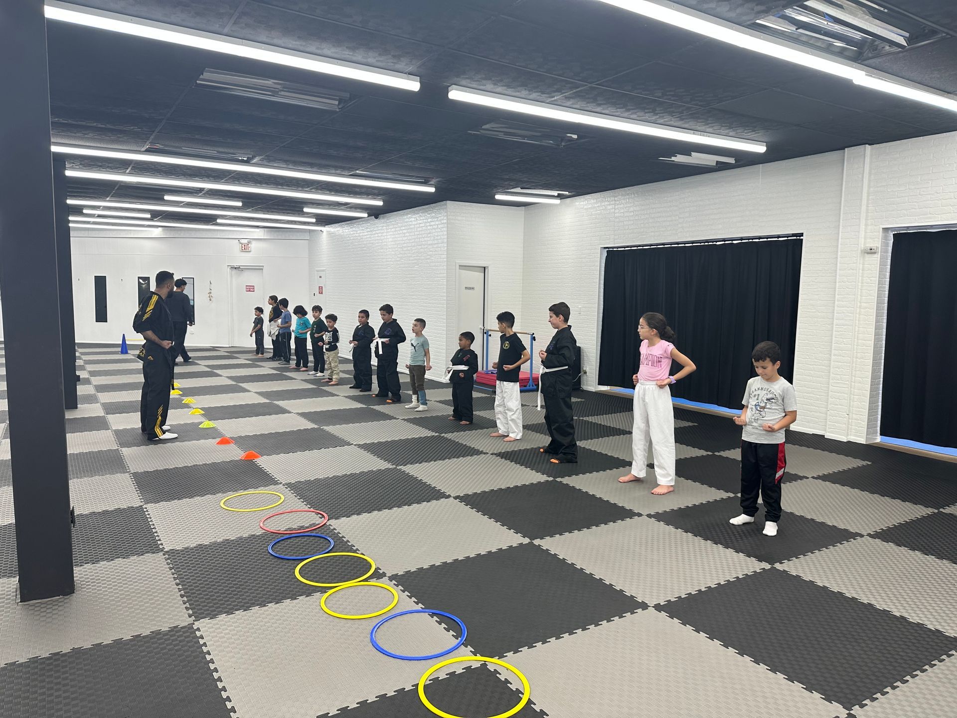 People lined up in a gym-like room beside colored rings on the floor, waiting for an activity.
