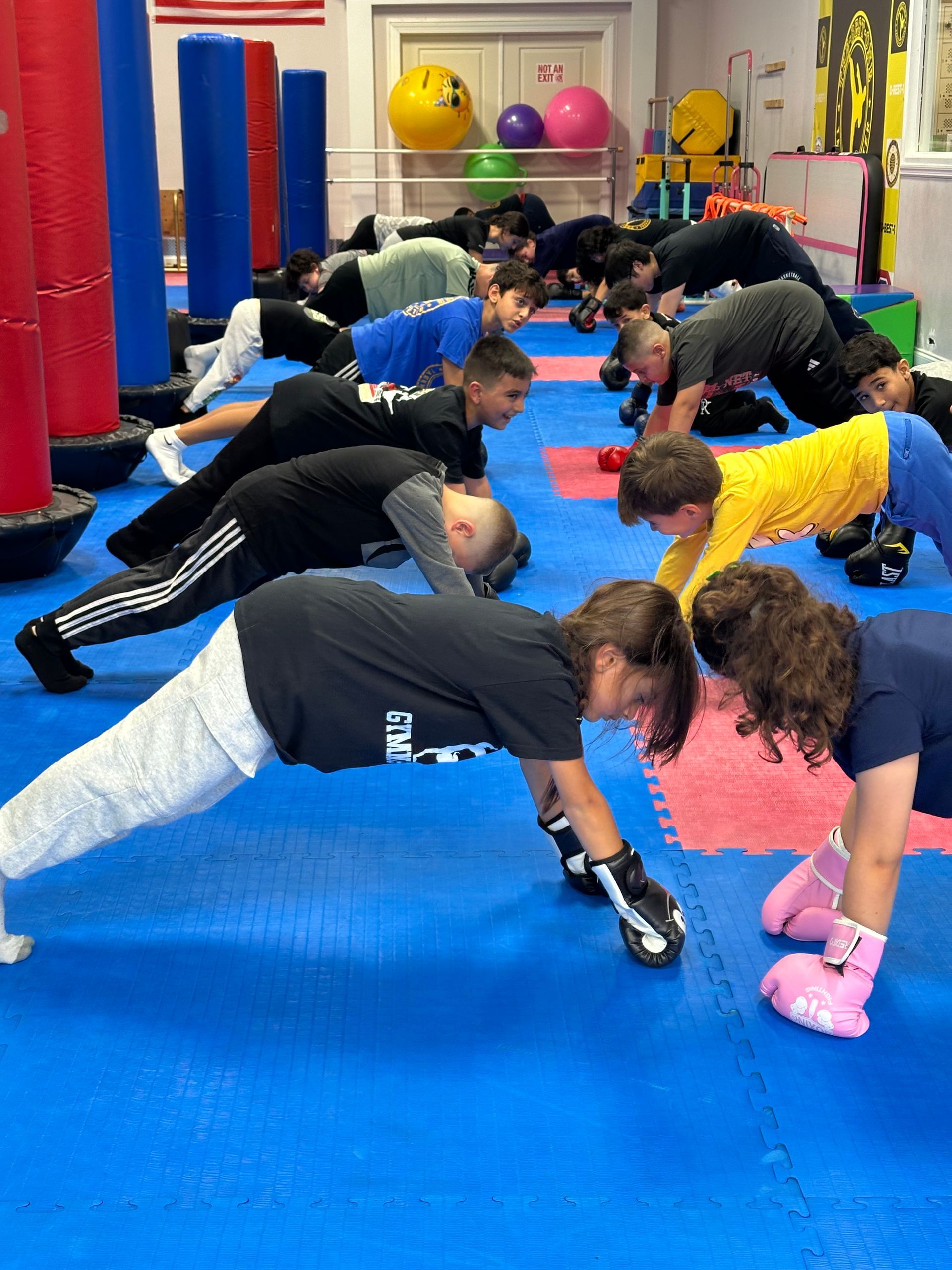 People exercising in a gym, holding plank positions on blue mats with colorful equipment in the background