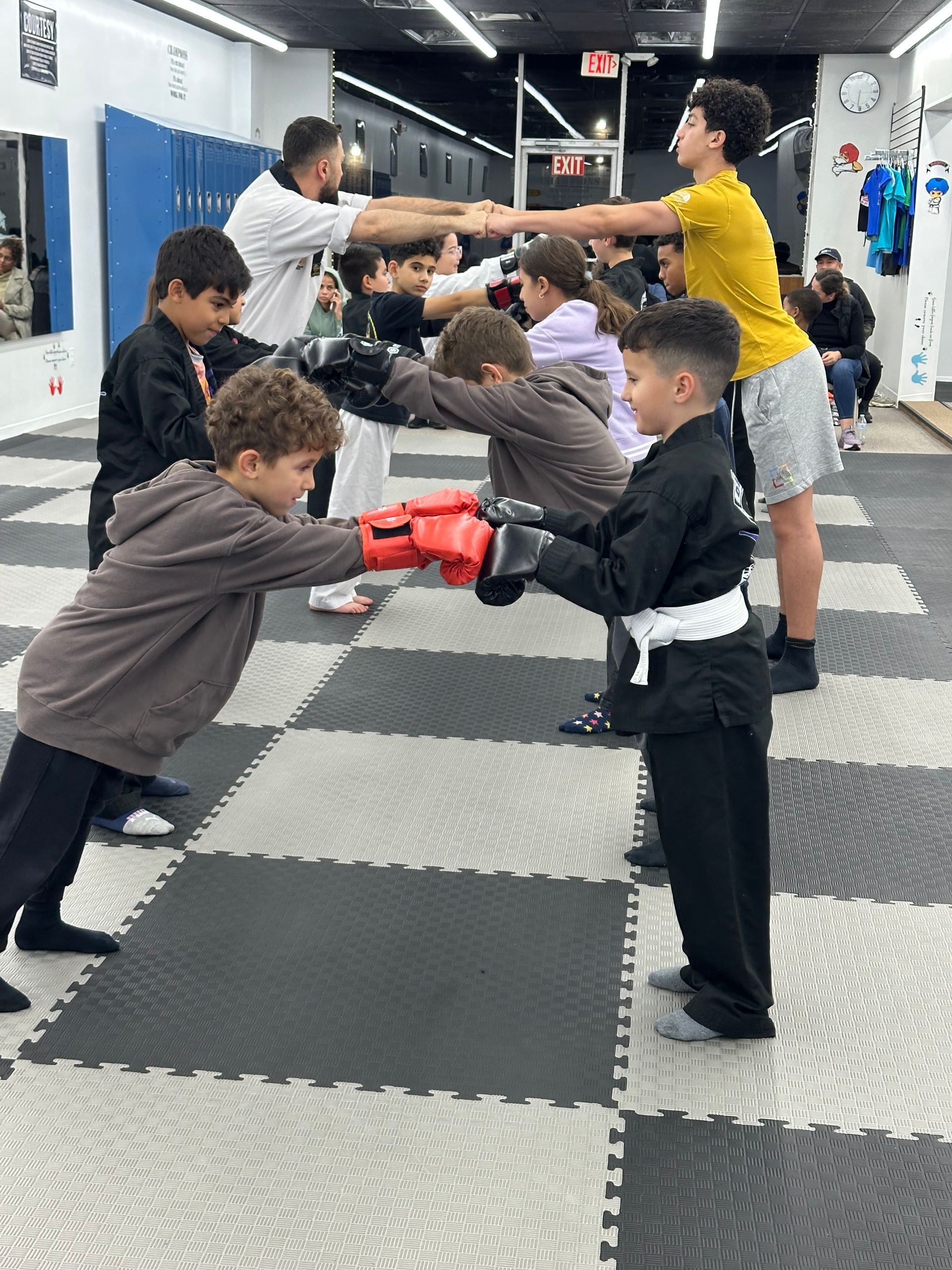 Children practicing partner drills with padded gloves in a martial arts studio