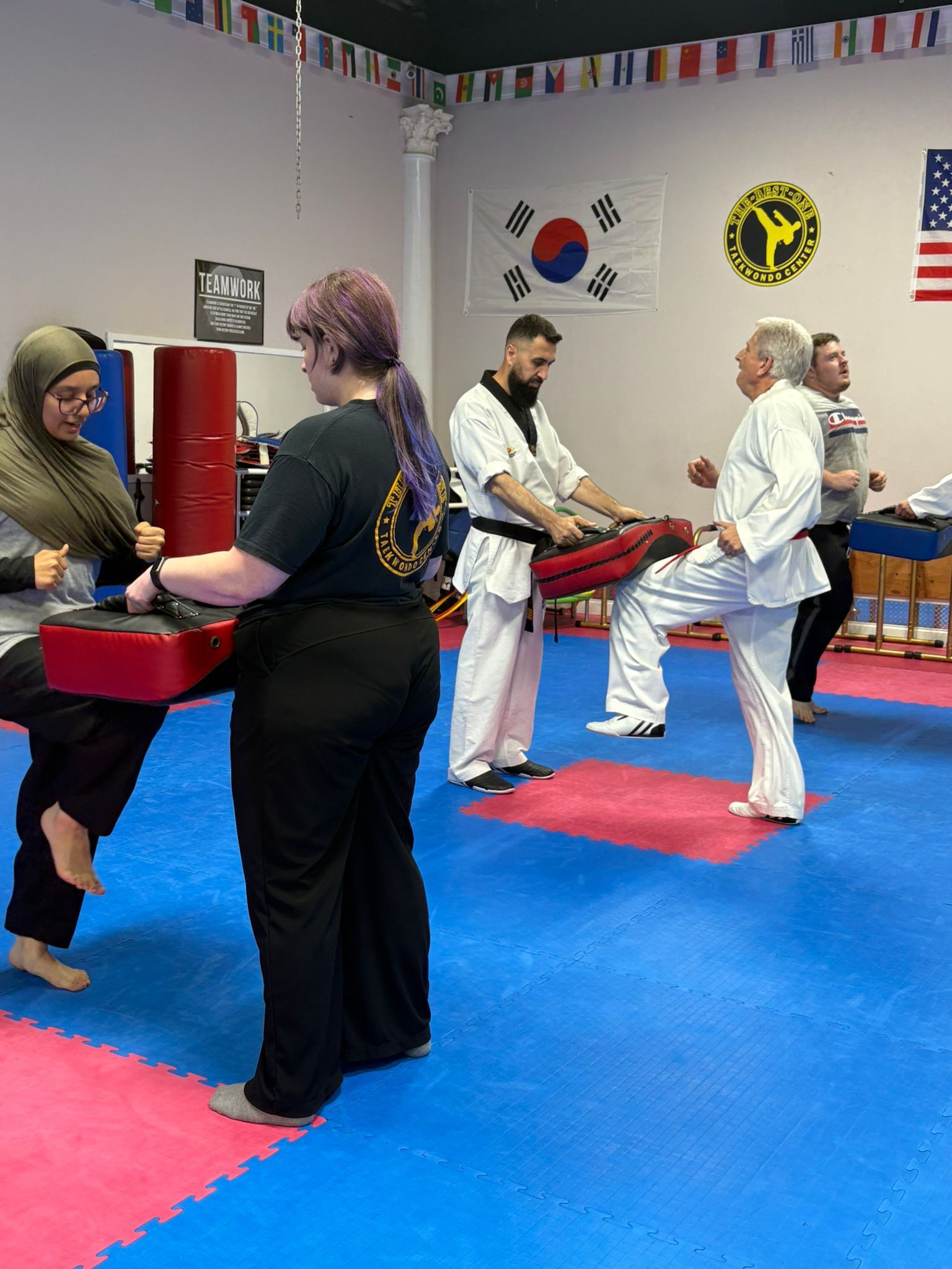 Martial arts class practicing partner drills on blue mats in a dojo with wall flags and emblems