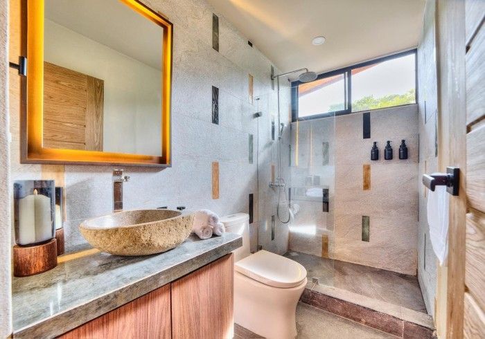 Bathroom with stone sink, shower, wood vanity, and patterned wall tiles. Natural light.