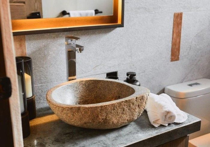 Stone sink with chrome faucet in a modern bathroom. White towel, candle, and soap dispenser are on the counter.