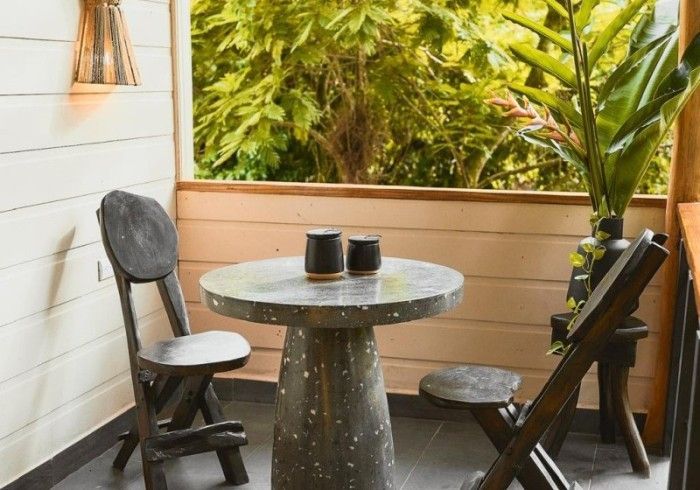 Small outdoor seating area with a gray table, black chairs, and lush green foliage in the background.