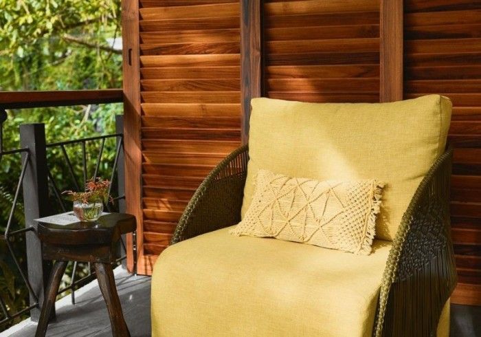 Cozy yellow armchair with patterned pillow on a wooden deck overlooking greenery.