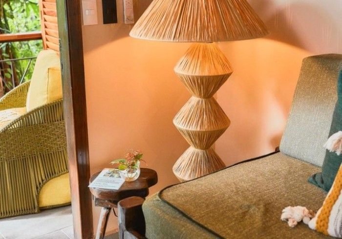 Rope-covered lamp near a sofa with green cushions and a small wooden table, and a balcony with a woven chair.