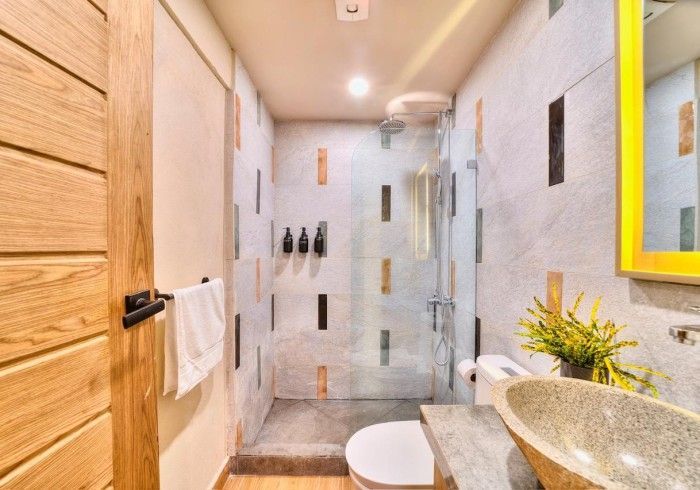 Bathroom with wood door, patterned tile, glass shower, stone sink, and yellow-framed mirror.