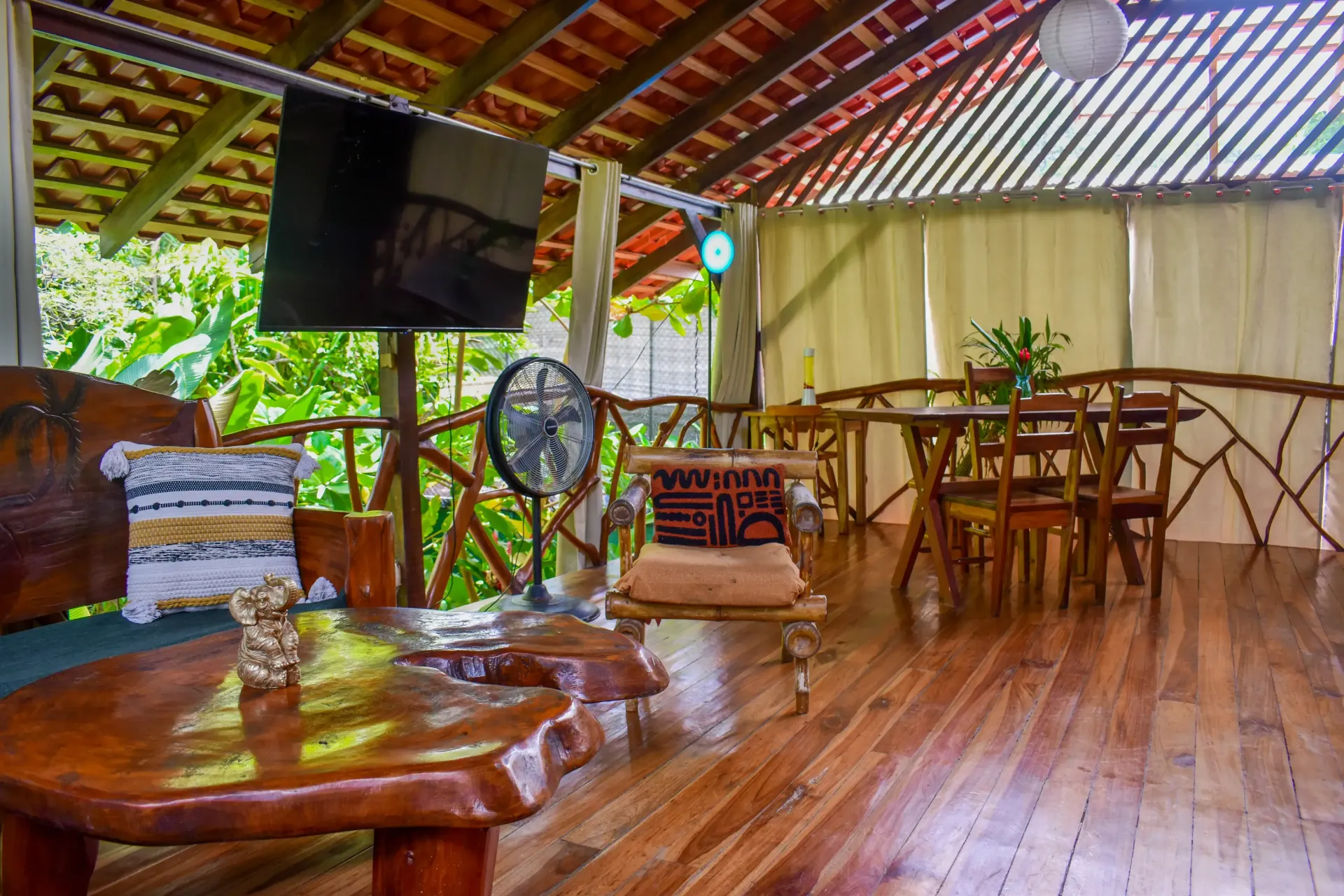 Wooden outdoor living space with furniture, TV, and dining table.