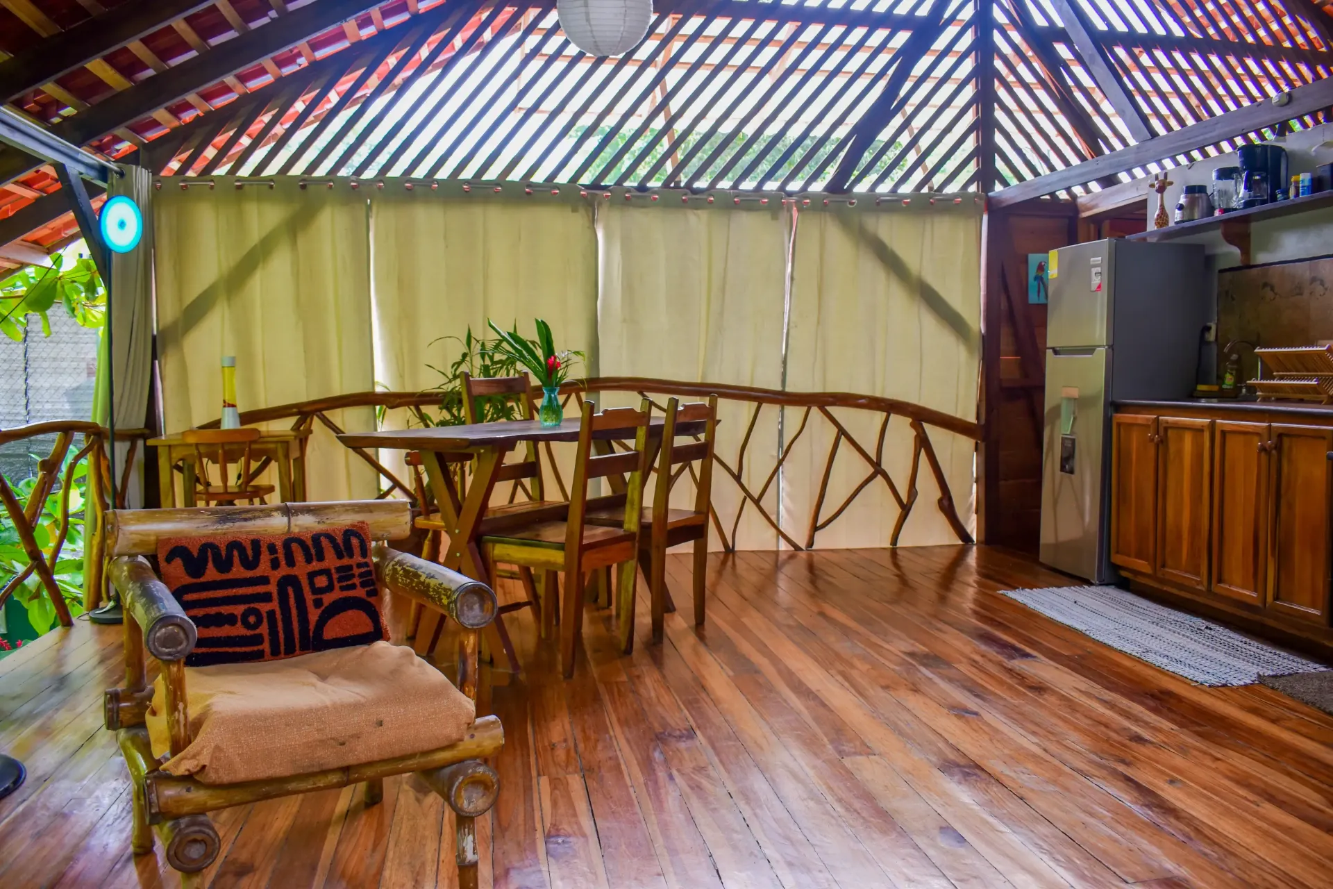 Wooden deck with a table, chairs, kitchen, and a decorative chair with a pillow.