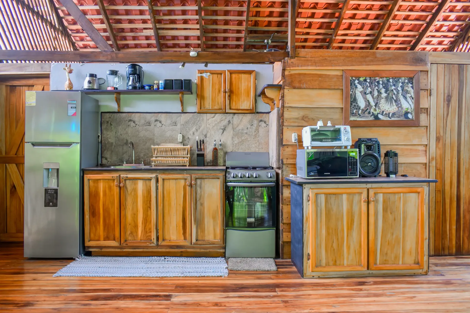 Kitchen with wooden cabinets, a refrigerator, stove, and appliances. Tile roof and wood walls.