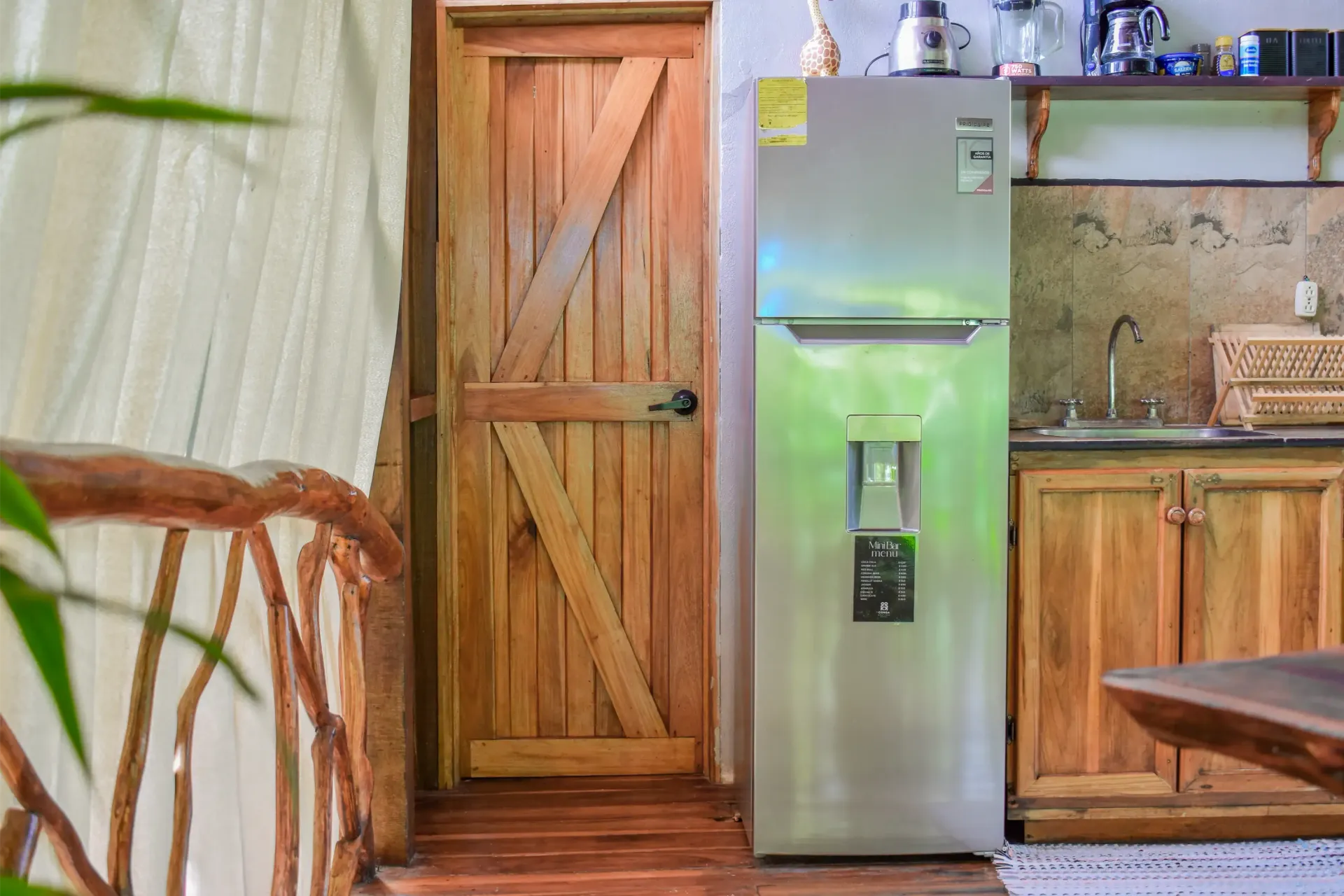 Wooden kitchen with fridge, cabinets, door, and a partially visible balcony.