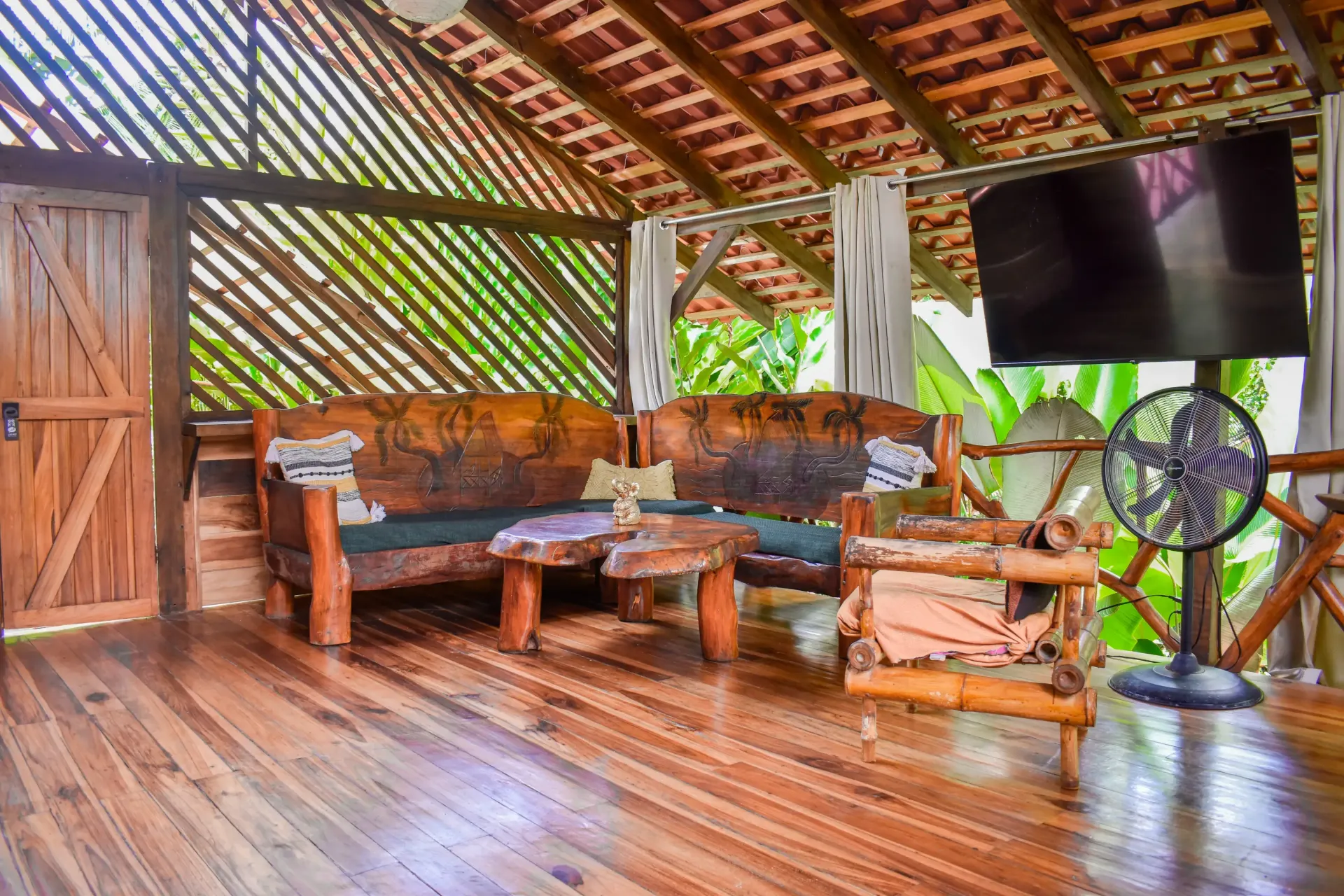 Wooden outdoor living room with a sofa, armchair, table, and TV.