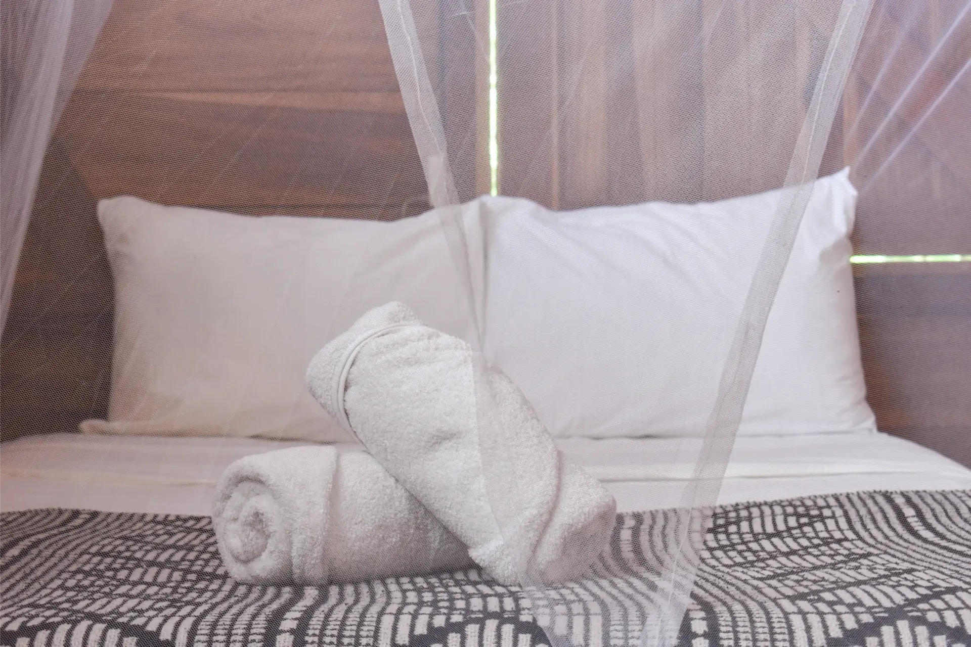 Bed with white linens, rolled towels, and a mosquito net.