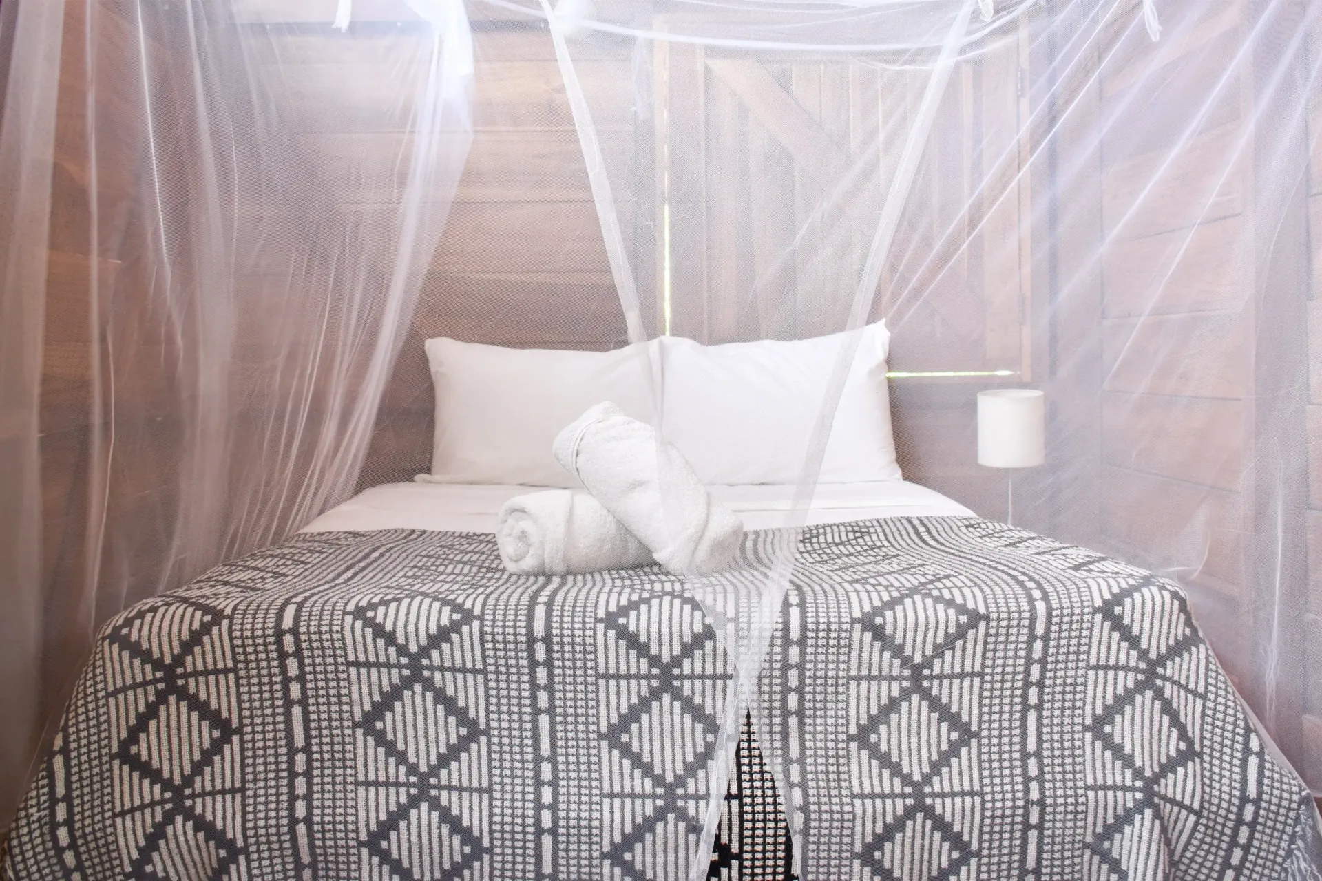 Bed with decorative quilt, white pillows, and mosquito netting.