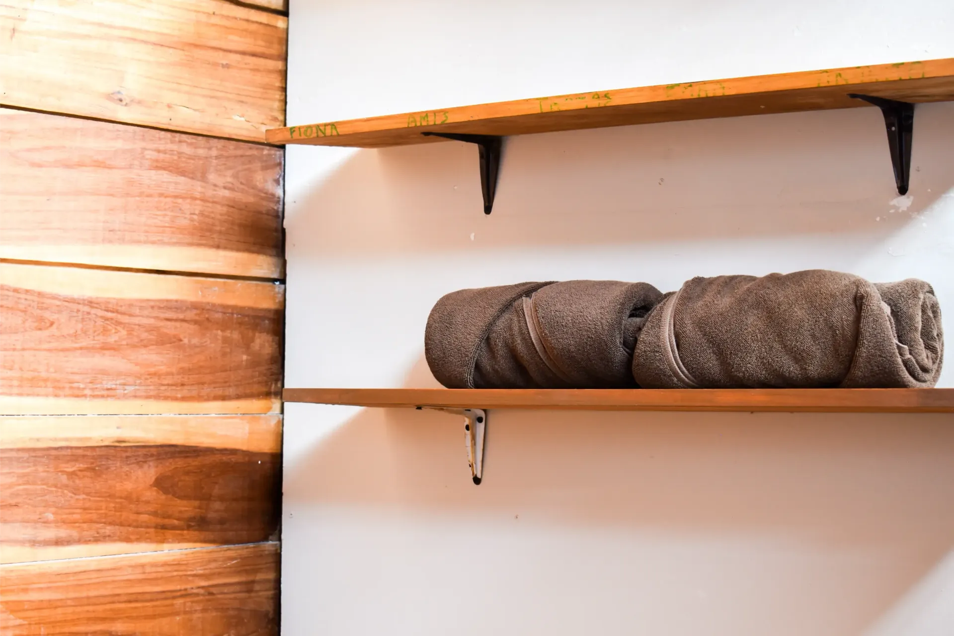 Wooden shelves on a white wall. Rolled brown towels rest on the bottom shelf.