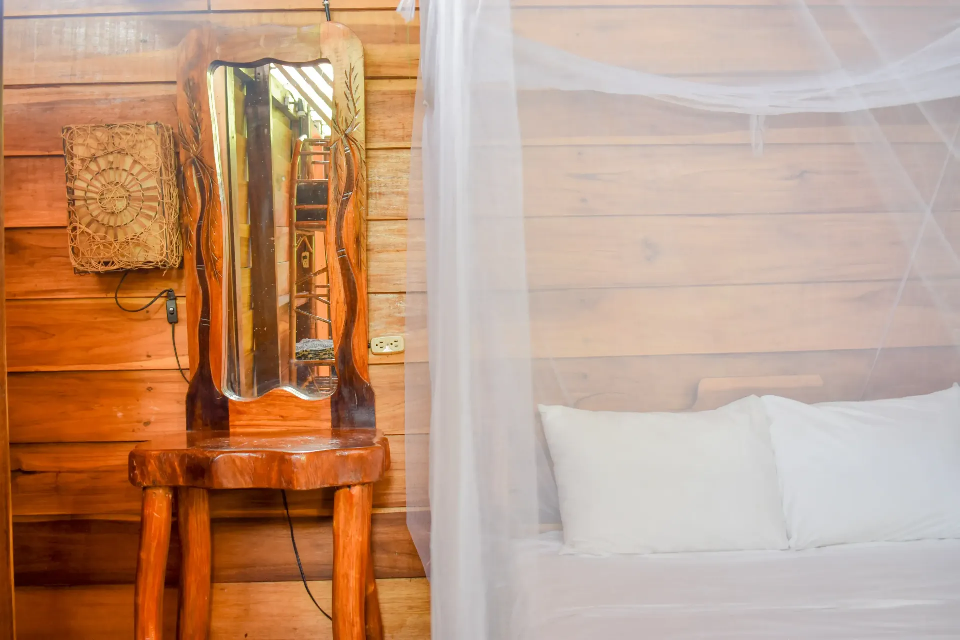 Wooden bedroom with a rustic vanity and bed with white linens and mosquito netting.