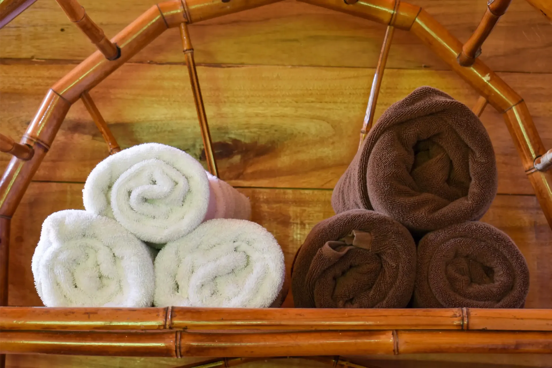 Rolled white and brown towels on bamboo shelf against a wood background.